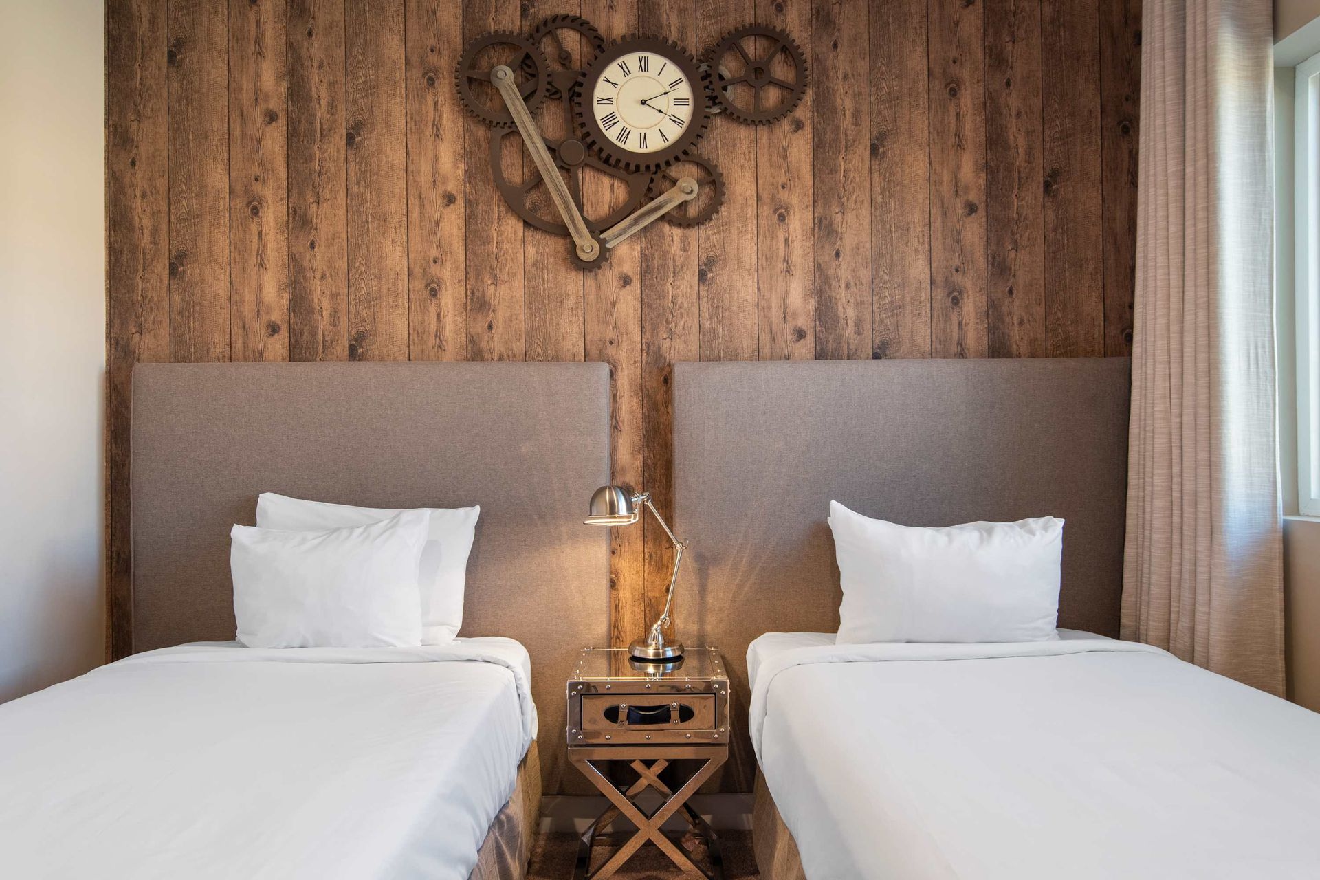 Cozy twin bedroom with rustic wood wall, unique clock decor, and warm inviting vibe.
