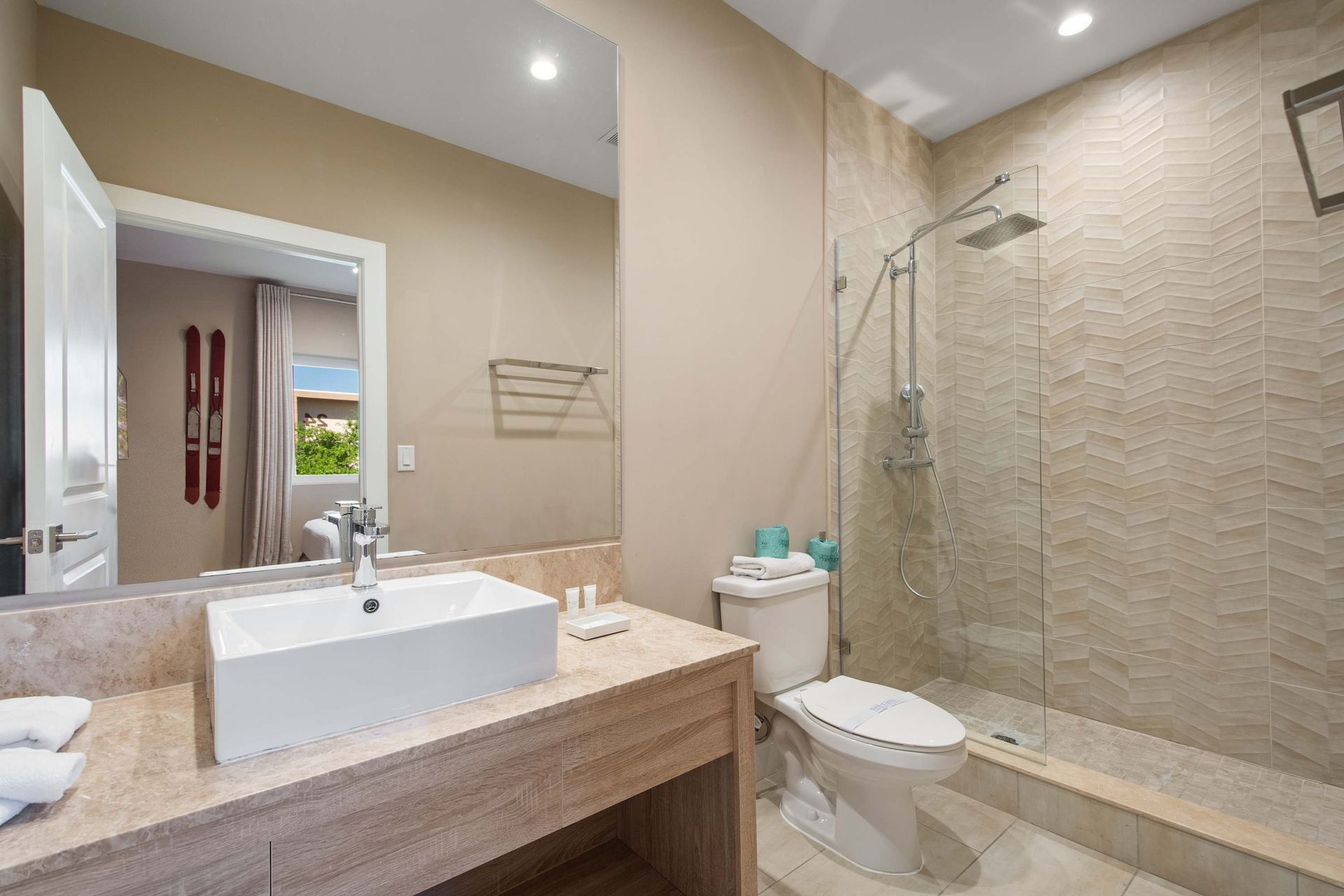 Elegant bathroom with glass walk-in shower, modern vanity, large mirror, and soft tones.
