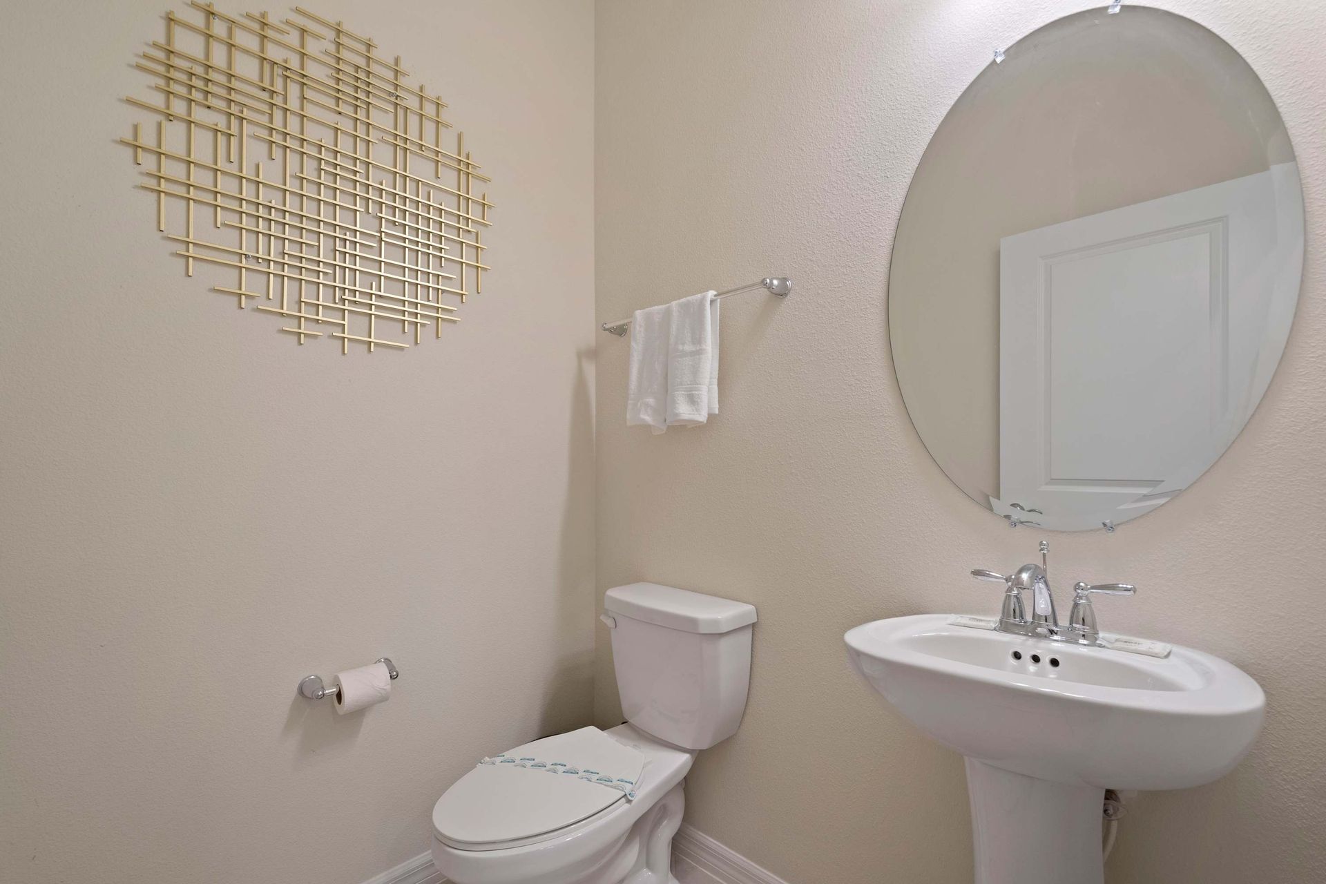 Bright and simple half bath with pedestal sink, round mirror, and modern wall art.
