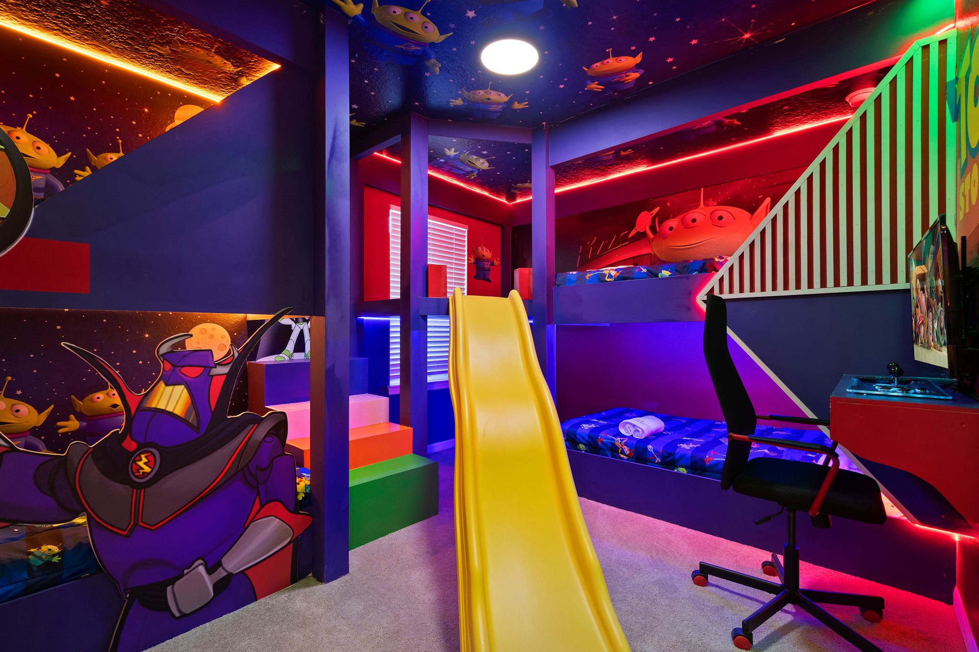 Galactic kids’ bunk room with slide, gaming setup, and space-themed lighting.
