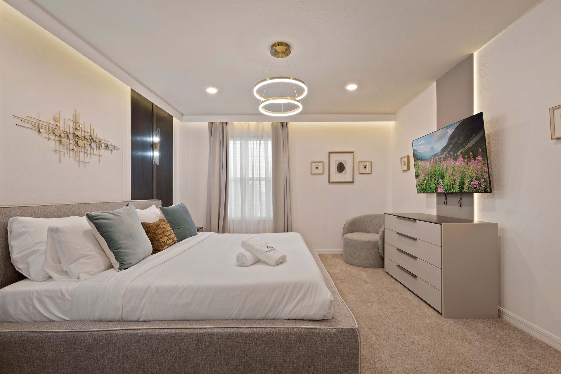 Spacious modern suite with king bed, smart TV, chic lighting, and cozy seating.
