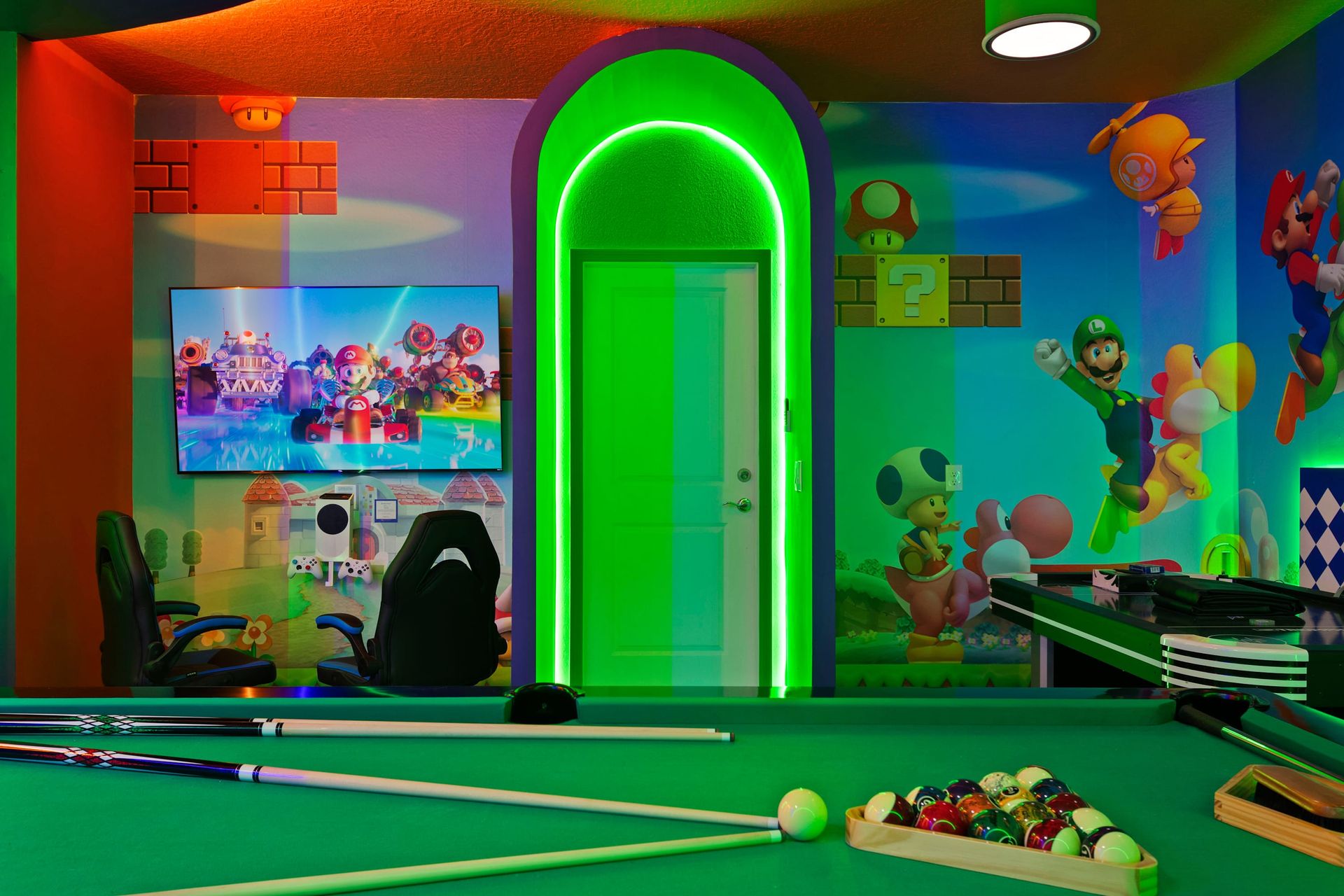 Neon-lit Super Mario game room with pool, gaming chairs, and vibrant murals.
