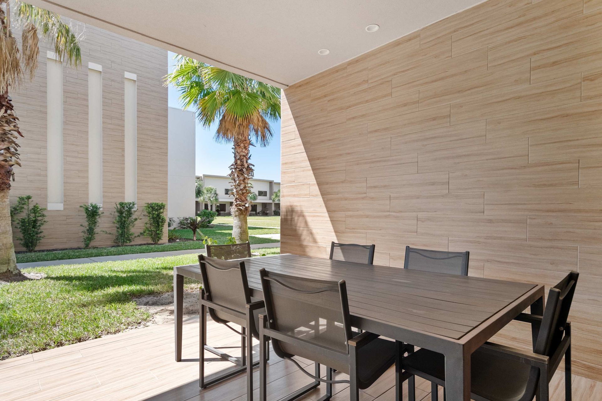 Covered patio with dining table, built-in grill, and views of green courtyard lawn.