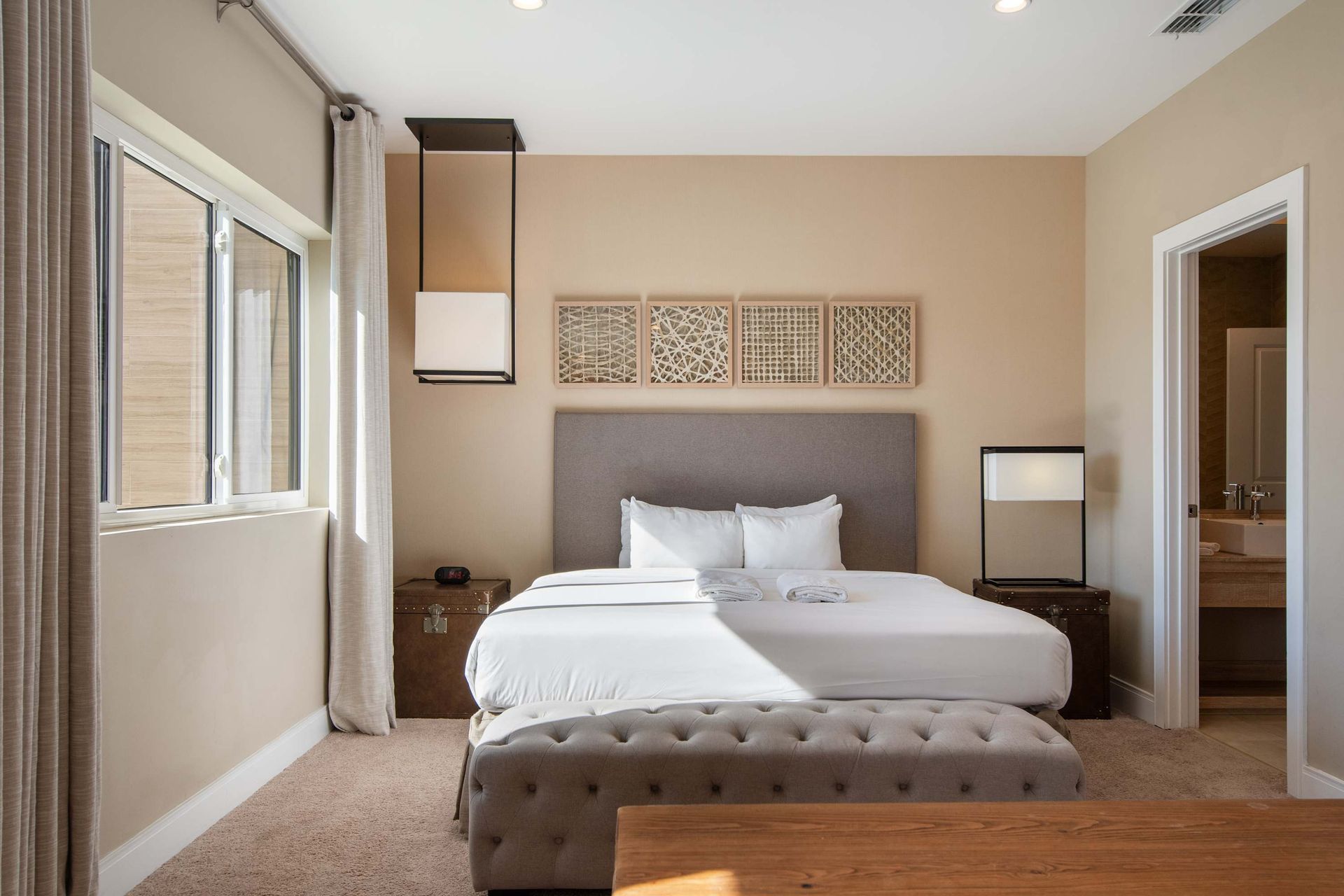 Elegant master bedroom with king bed, ensuite bathroom, bright windows, and bench.