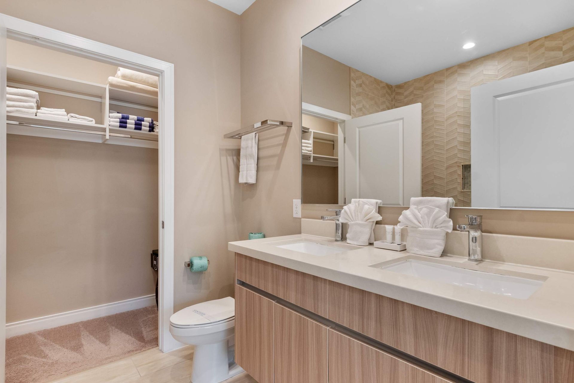Modern bathroom with spacious vanity, walk-in closet, large mirror, and warm decor.