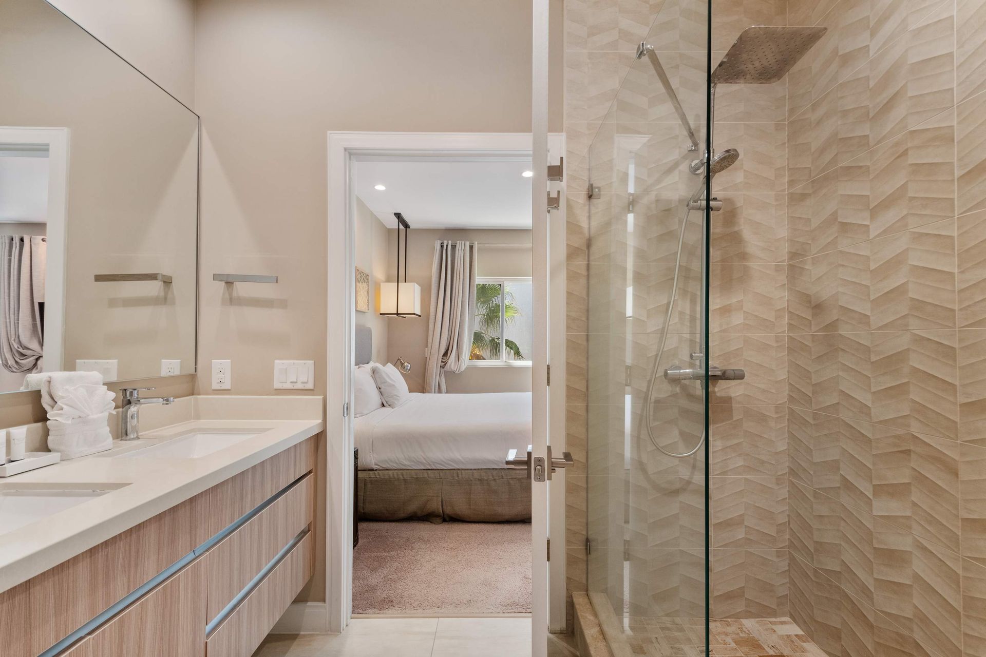 Elegant bathroom with glass walk-in shower, modern vanity, large mirror, and soft tones.