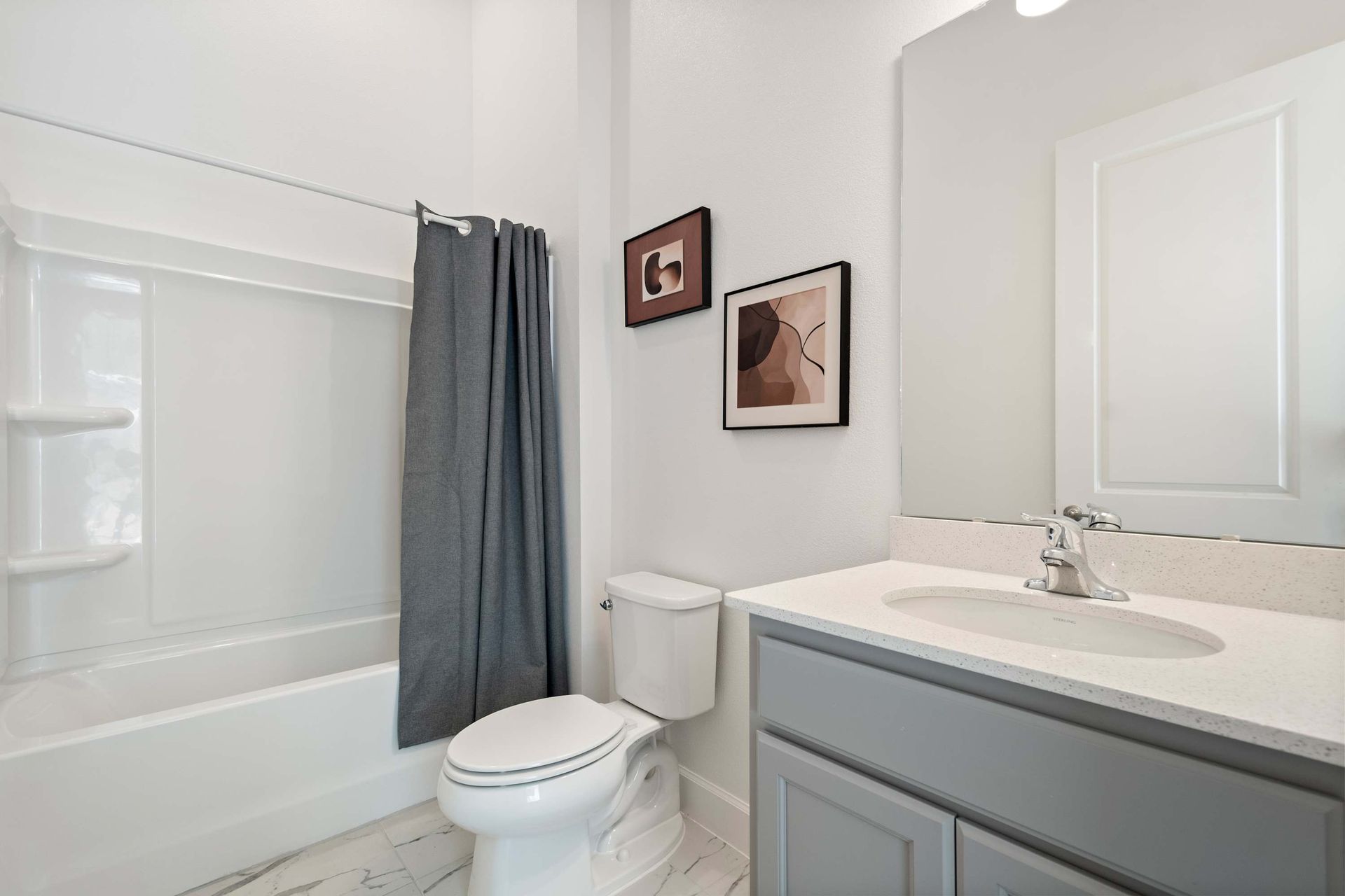 Clean and modern bathroom with sleek gray vanity, tub/shower combo, and soft lighting
