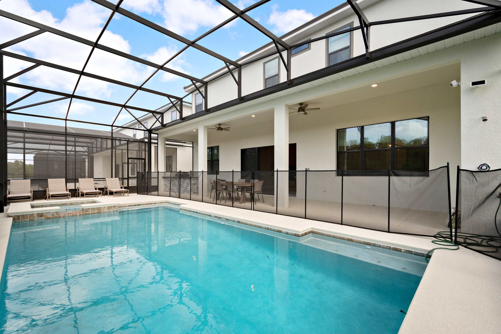 Spacious screened-in pool area with safety fence, loungers, and covered patio dining
