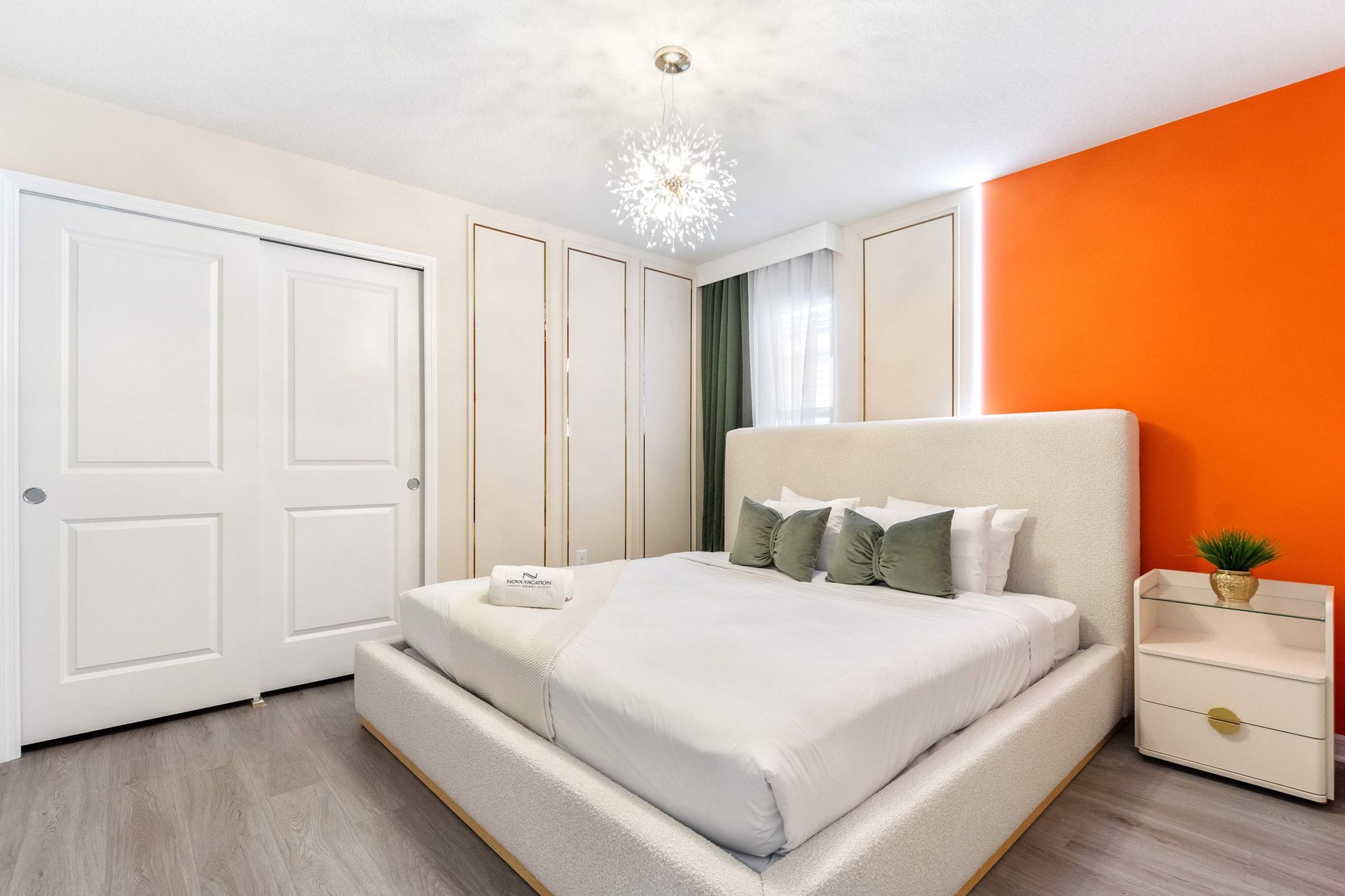 Bright and elegant bedroom with bold orange accent wall and designer lighting.