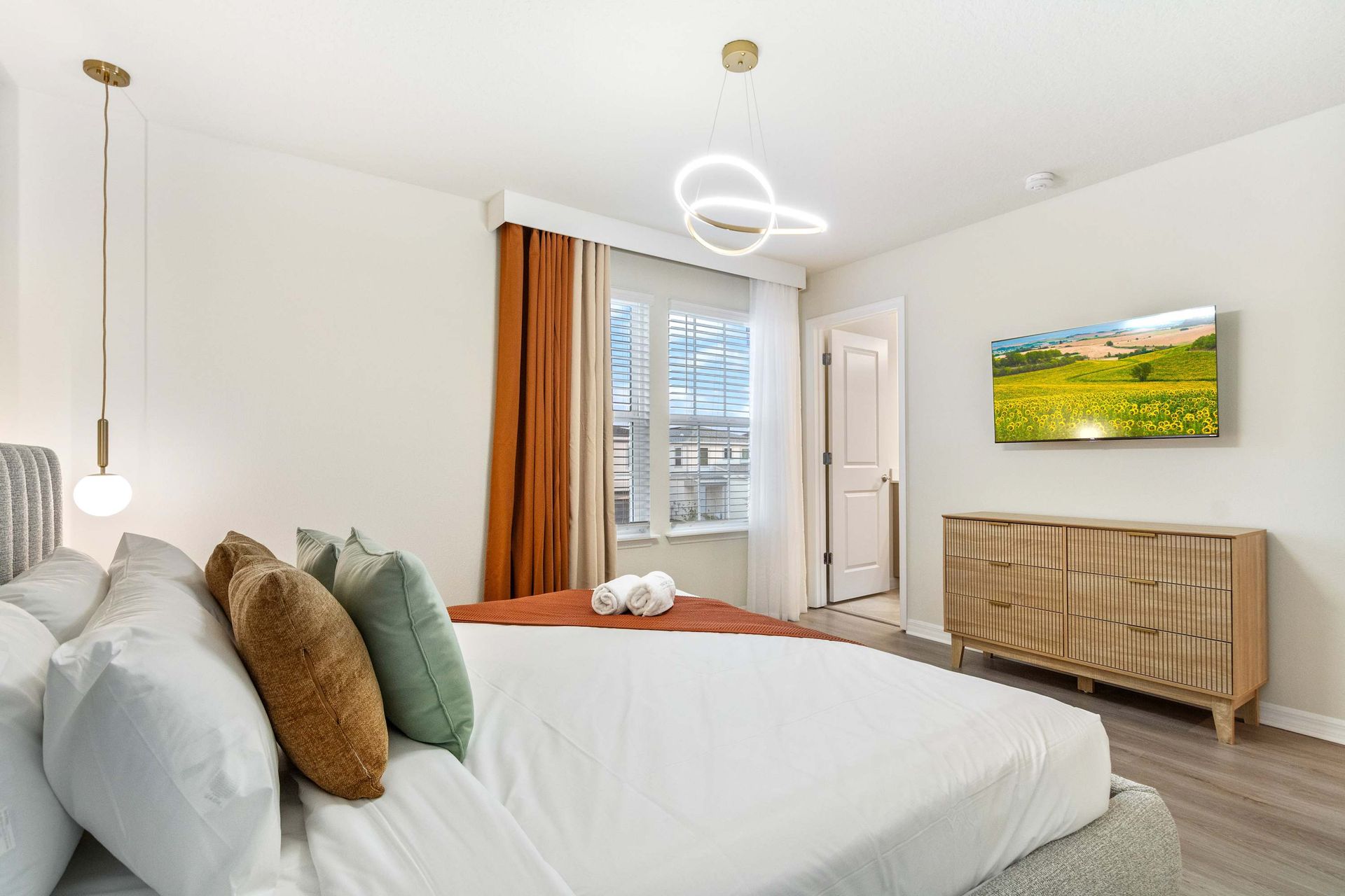 Bright and airy bedroom with modern lighting, cozy linens, and smart TV comfort.