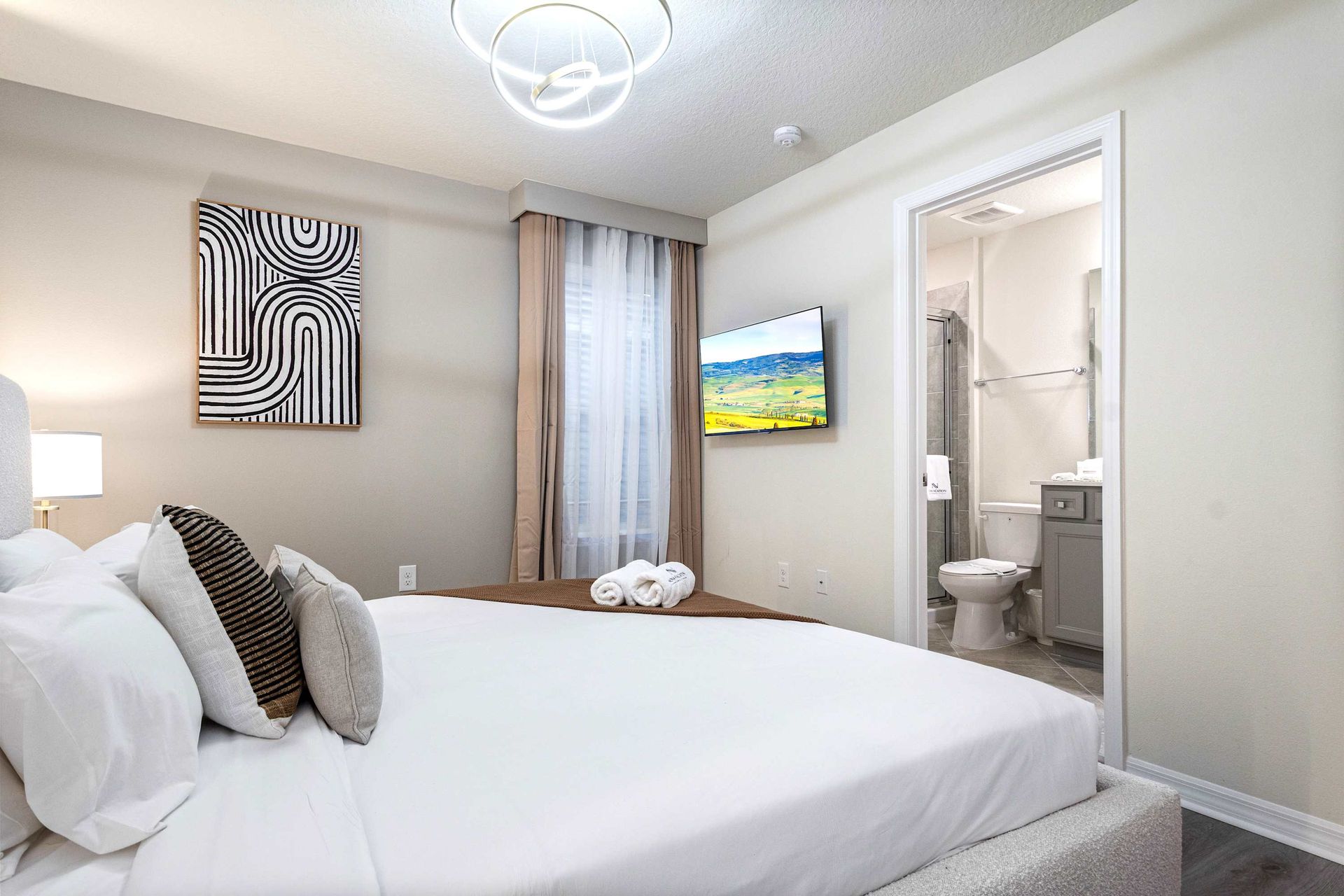Modern ensuite bedroom with sleek lighting, cozy linens, and a wall-mounted TV.
