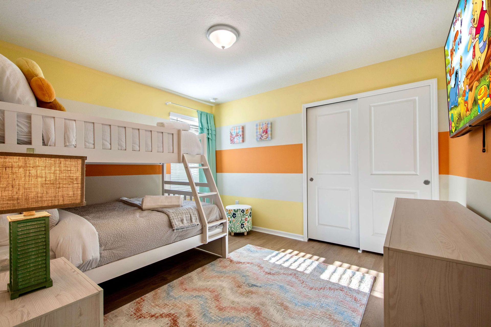 Bright and playful bunk room with smart TV, colorful decor, and cozy bedding.
