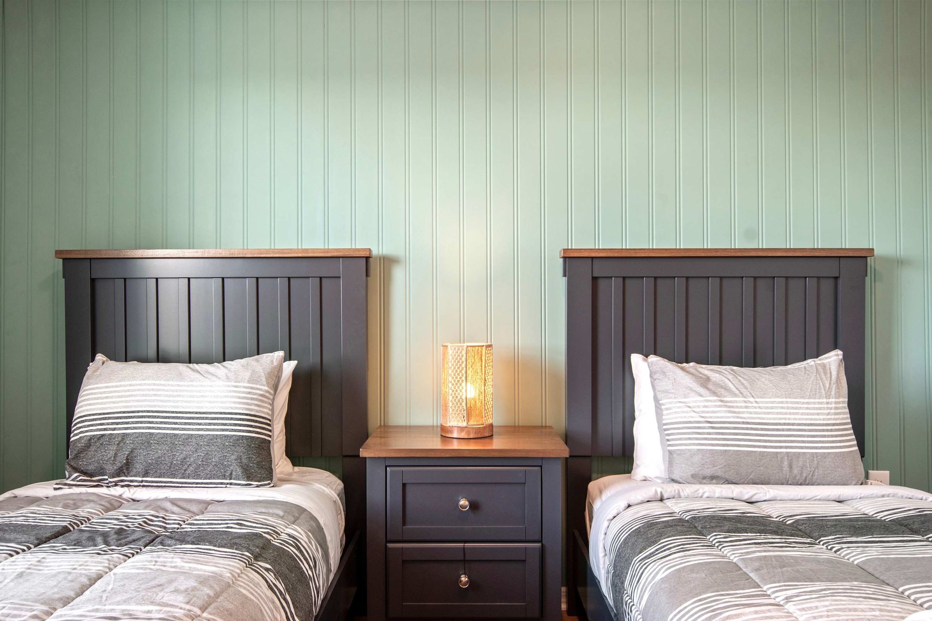 Cozy twin bedroom with matching beds, warm lighting, and a calming green backdrop.
