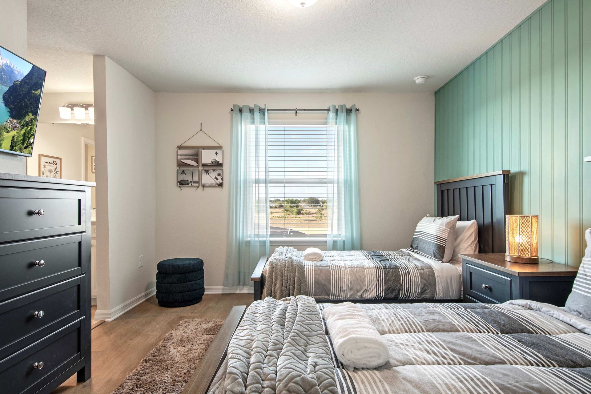 Charming twin room with soft lighting, green accent wall, and streaming-ready TV.
