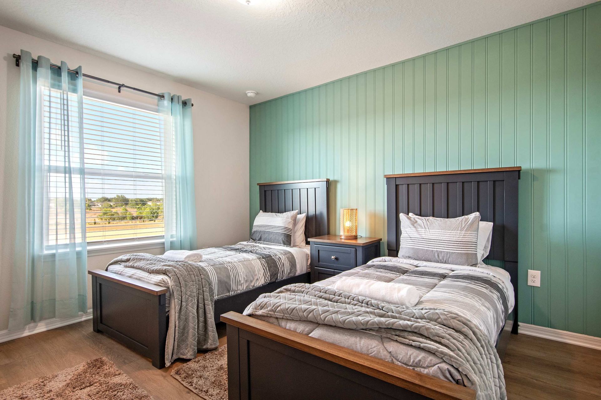 Bright twin room with cozy bedding, wood accents, and peaceful green feature wall.
