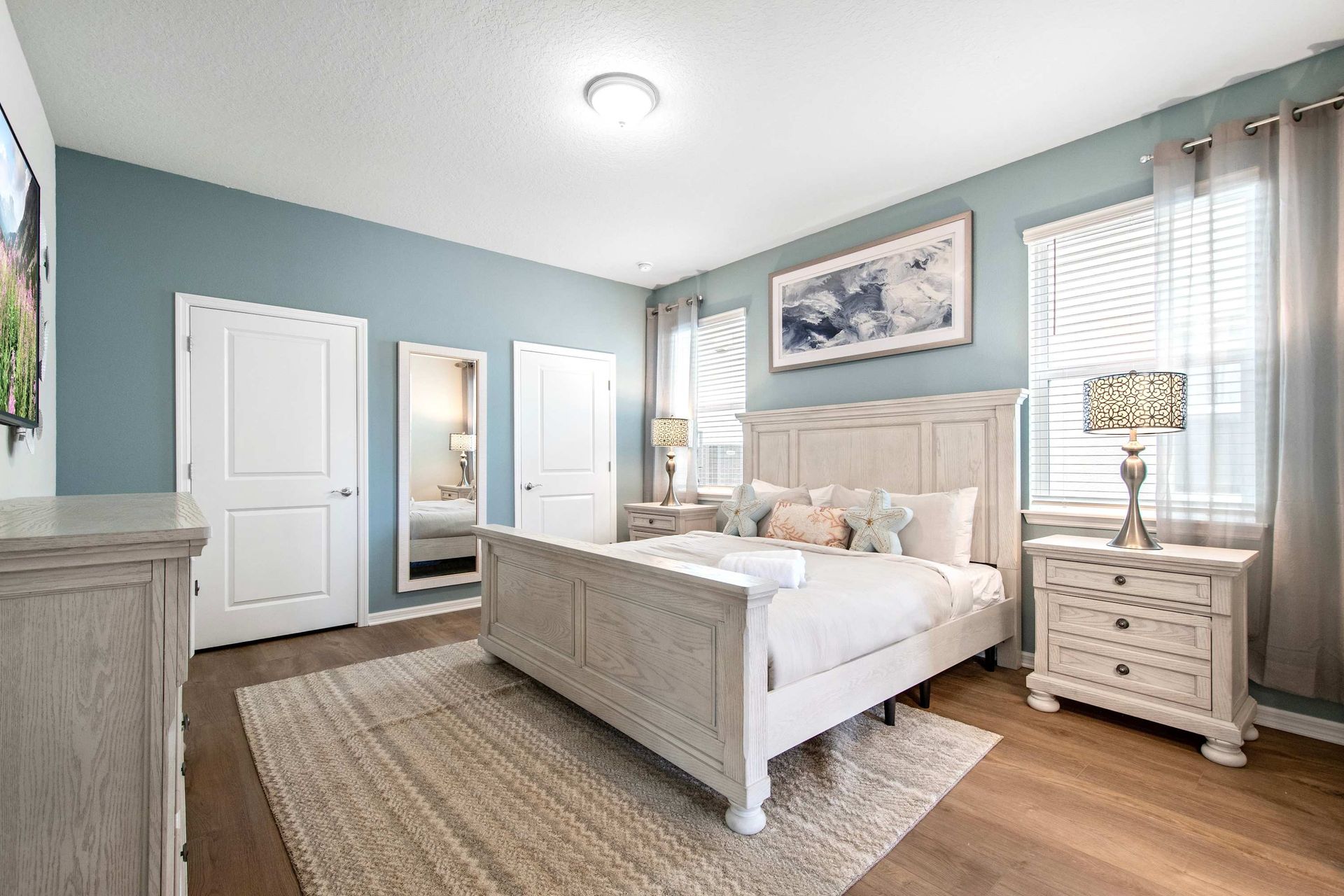 Serene primary suite with soft blue walls, elegant furnishings, and natural light.

