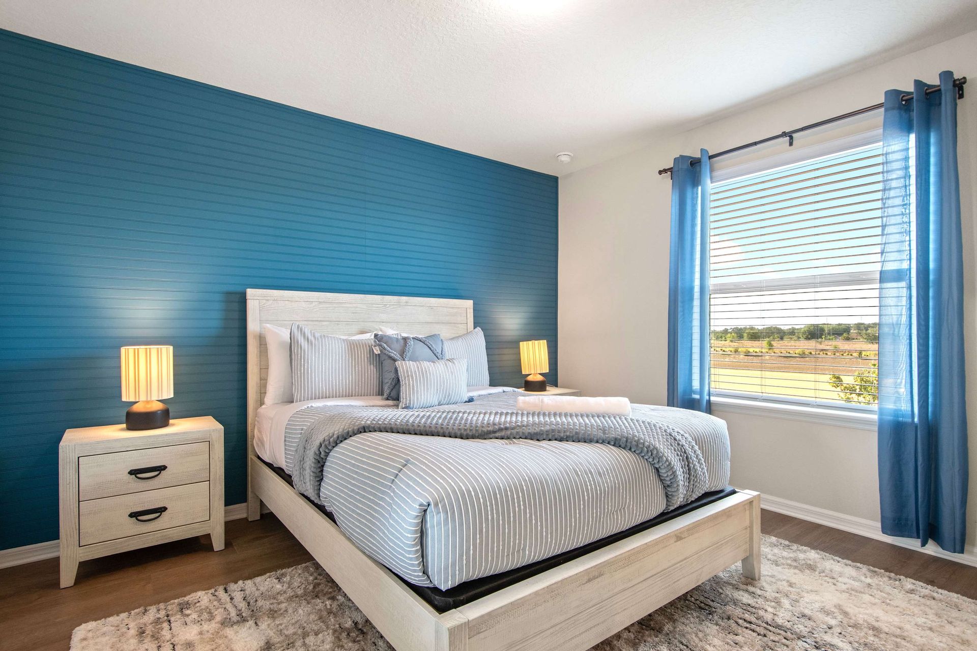 Bright guest room with bold blue accent wall, queen bed, and sunny window view.
