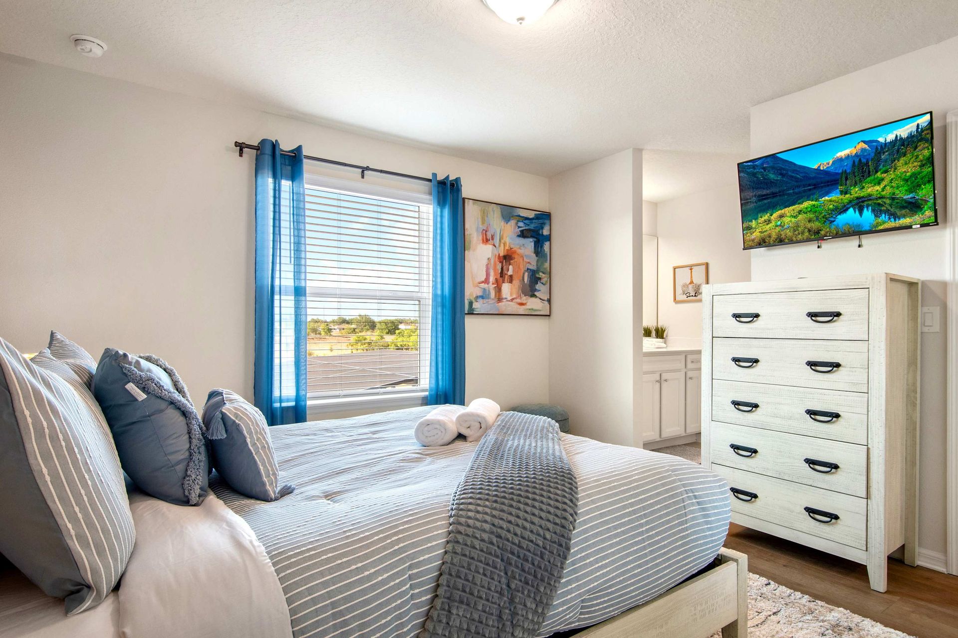 Inviting queen bedroom with smart TV, stylish blue accents, and ensuite access.
