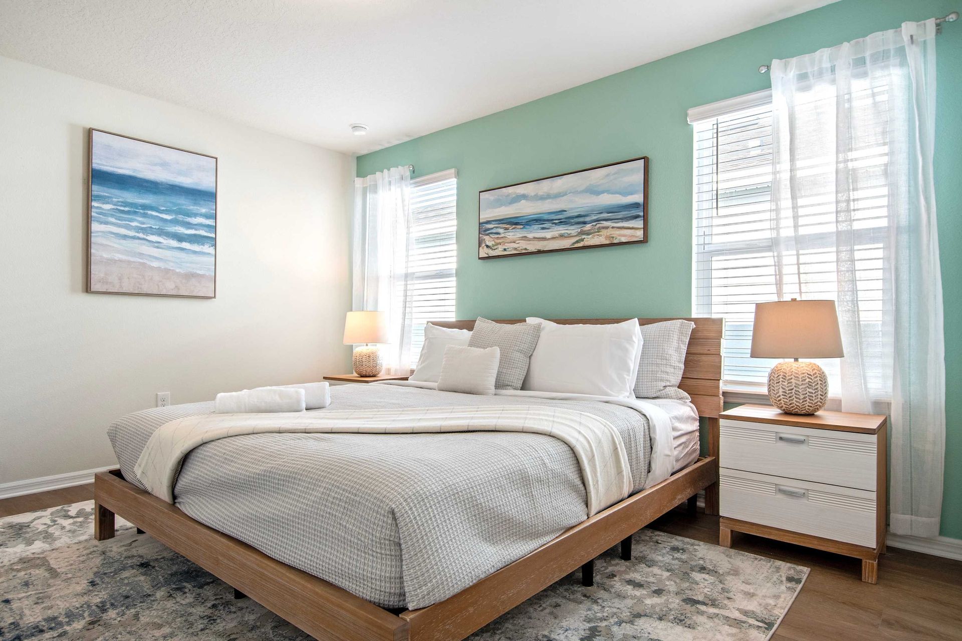 Coastal-inspired king bedroom with soft tones, beachy decor, and abundant sunlight.
