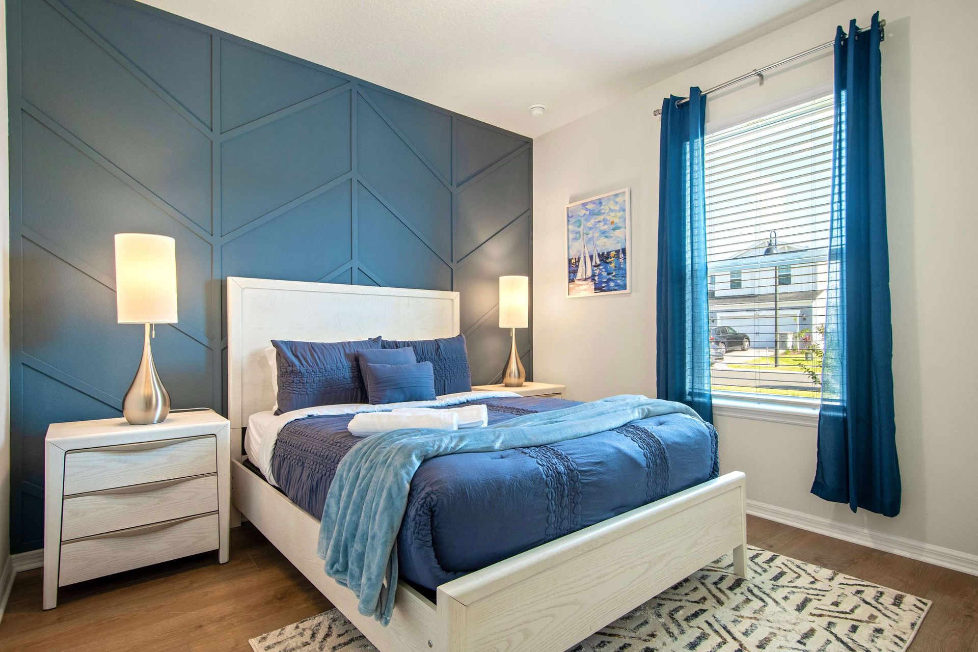 Modern queen bedroom with bold accent wall, rich blue tones, and natural light.
