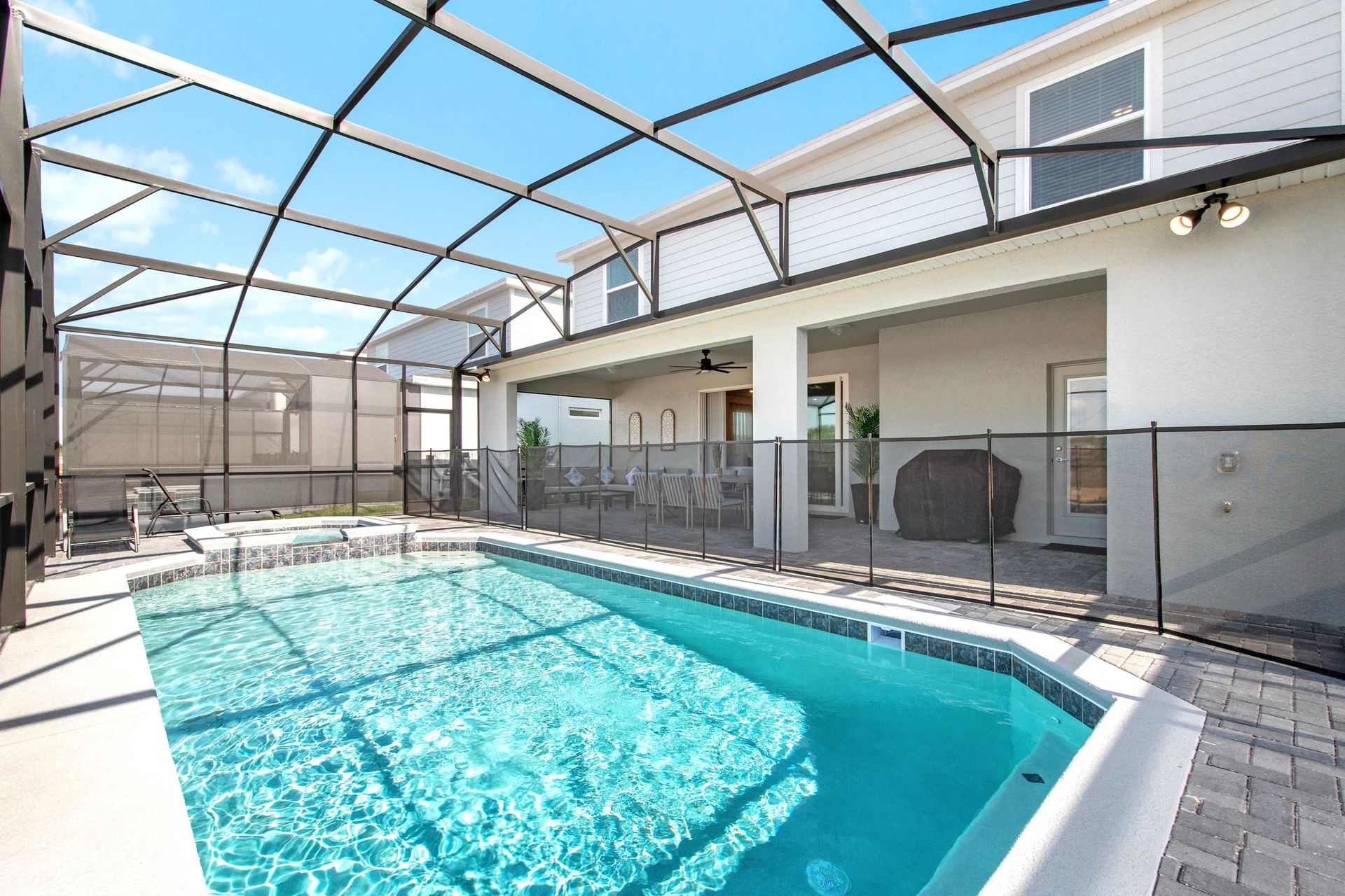 Screened-in private pool with safety fence, shaded patio, and sunny lounging area.
