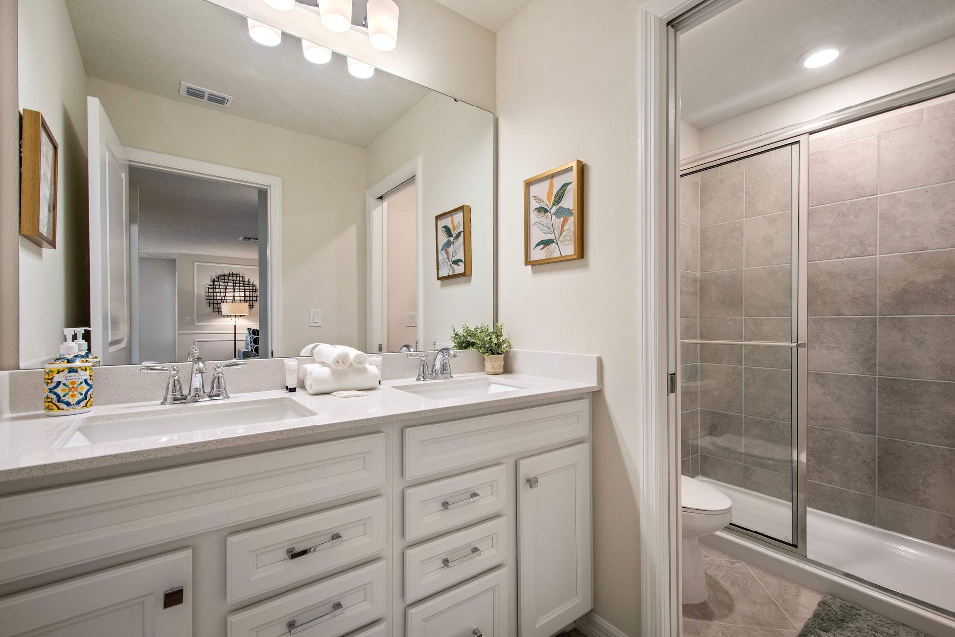 Modern bathroom with dual sinks, large mirror, and sleek glass-enclosed shower.
