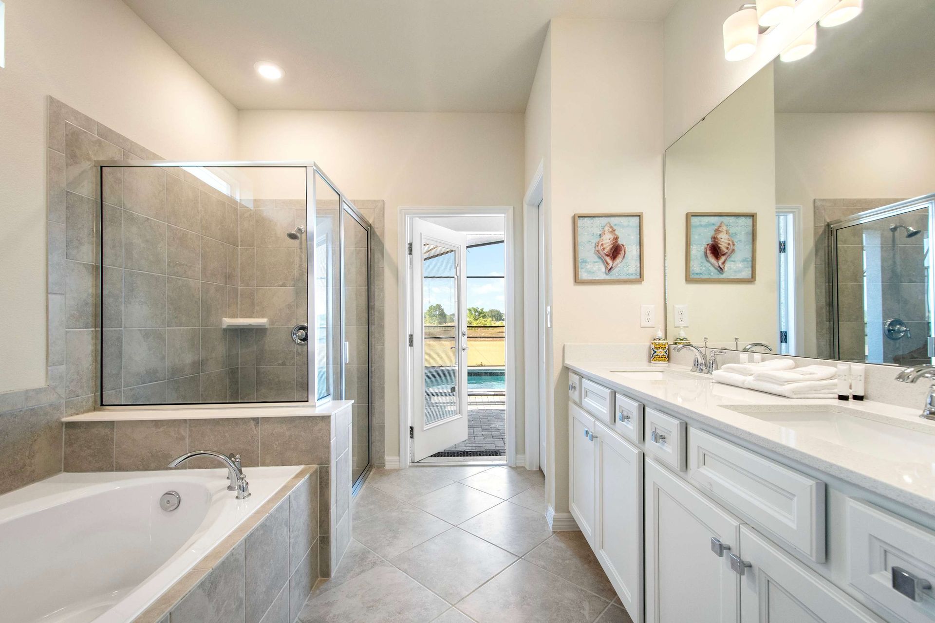 Luxurious ensuite with soaking tub, glass shower, double vanity, and pool access.
