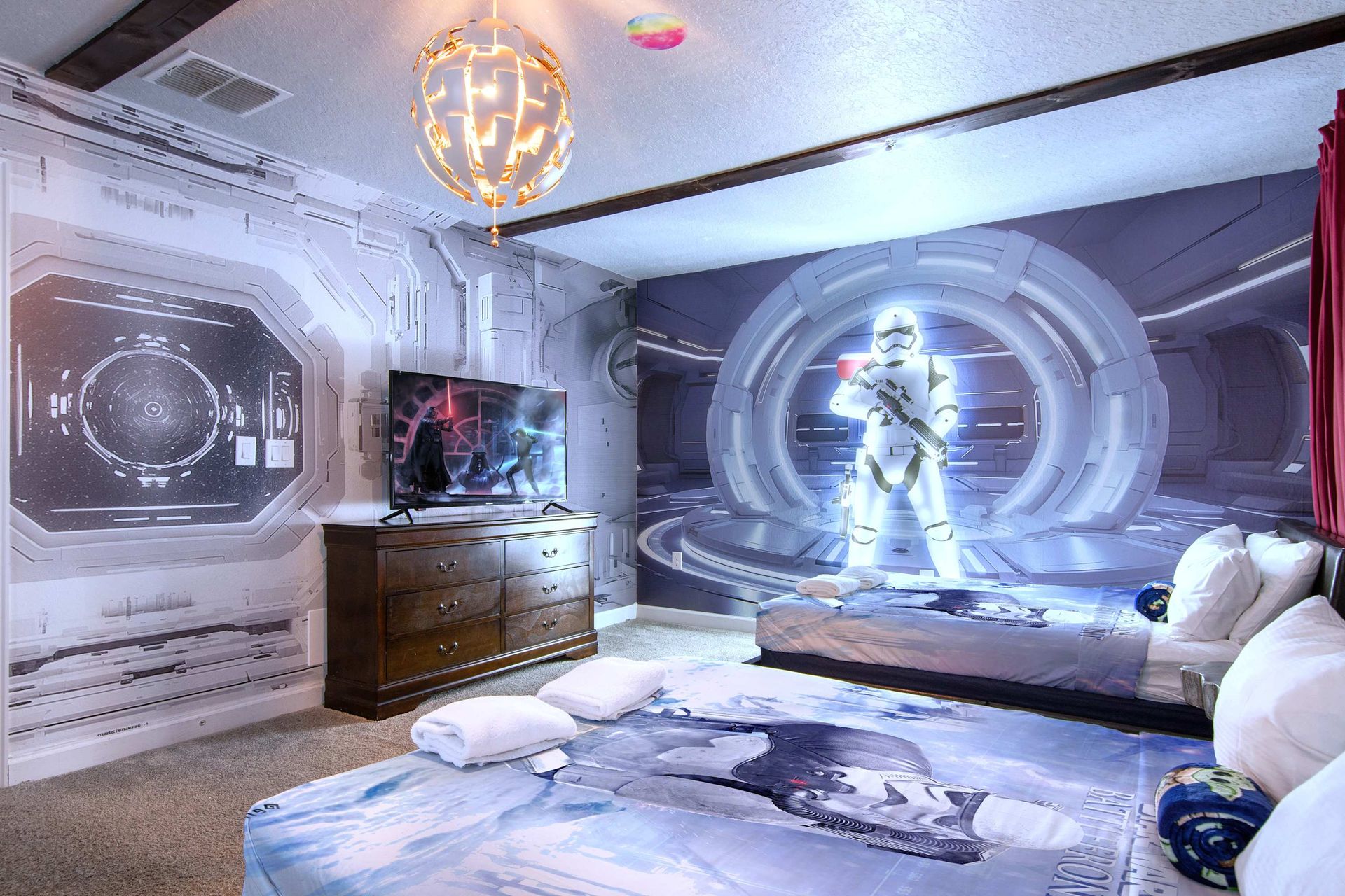 Immersive space adventure room with astronaut mural, smart TV, and comfy beds.
