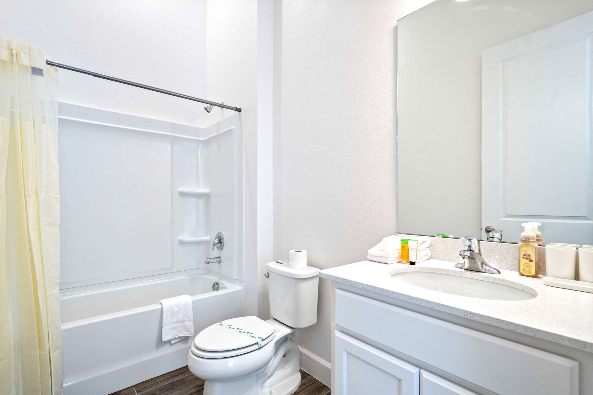 Bright and clean full bathroom with tub, large mirror, and modern white finishes
