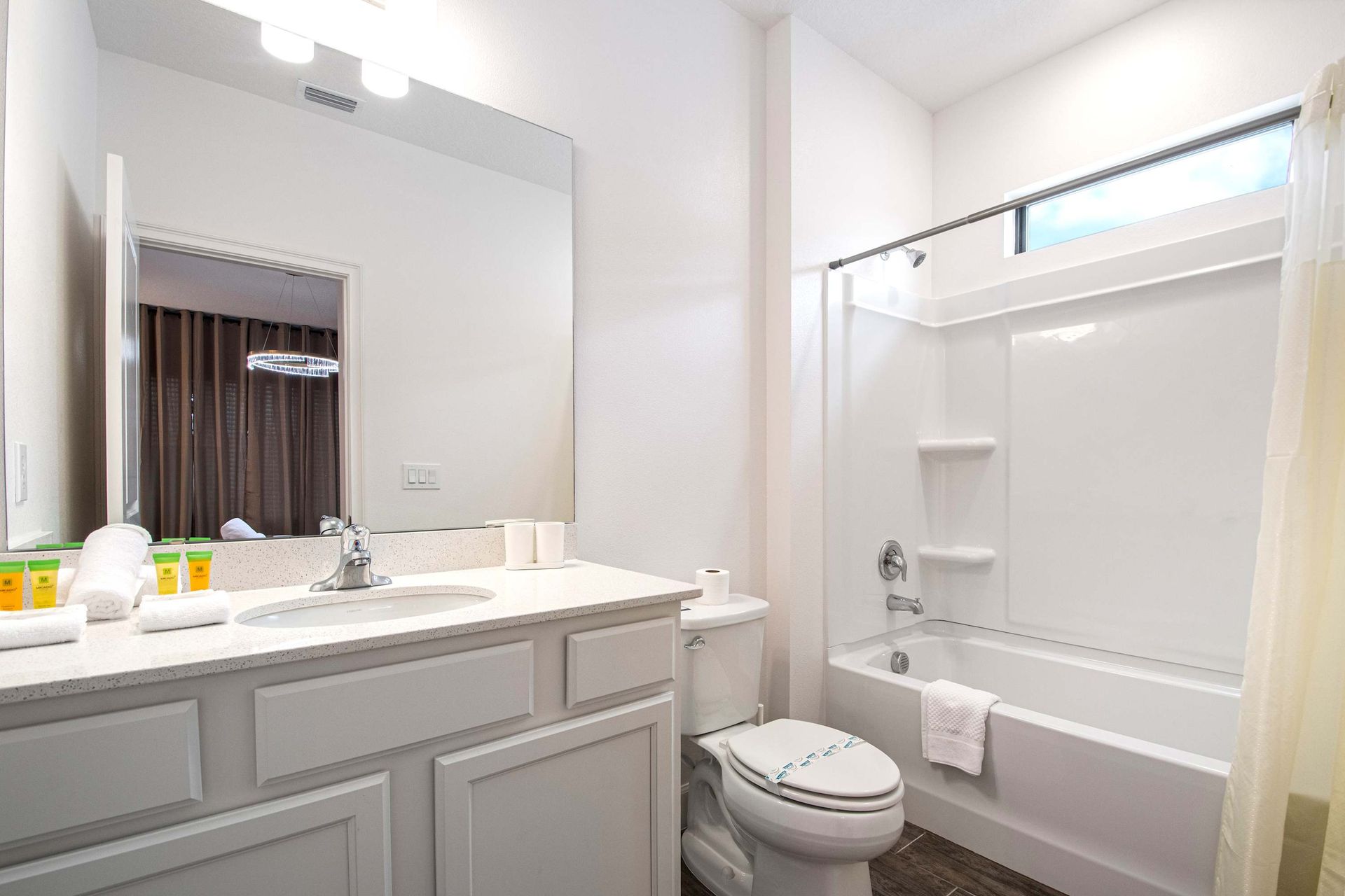 Clean and bright bathroom with tub, large vanity, and natural light above shower
