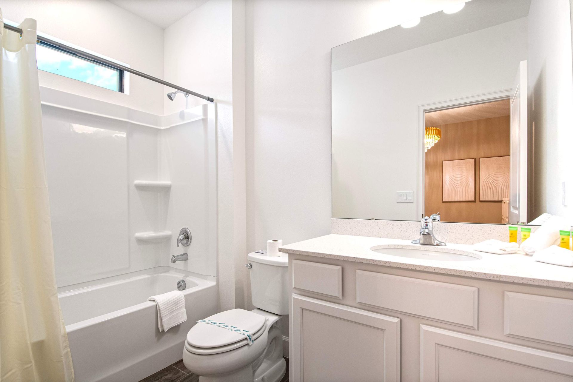 Clean and bright bathroom with tub, large vanity, and natural light above shower
