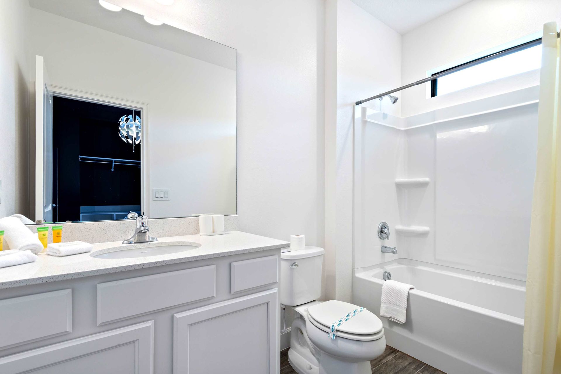 Clean and bright bathroom with tub, large vanity, and natural light above shower

