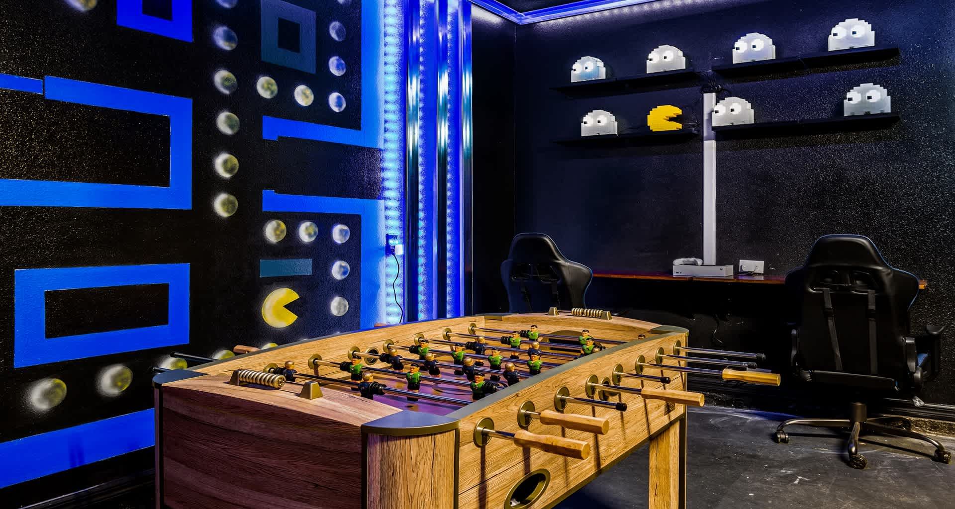 Retro gaming room with foosball, neon Pac-Man walls, and dual gaming stations!
