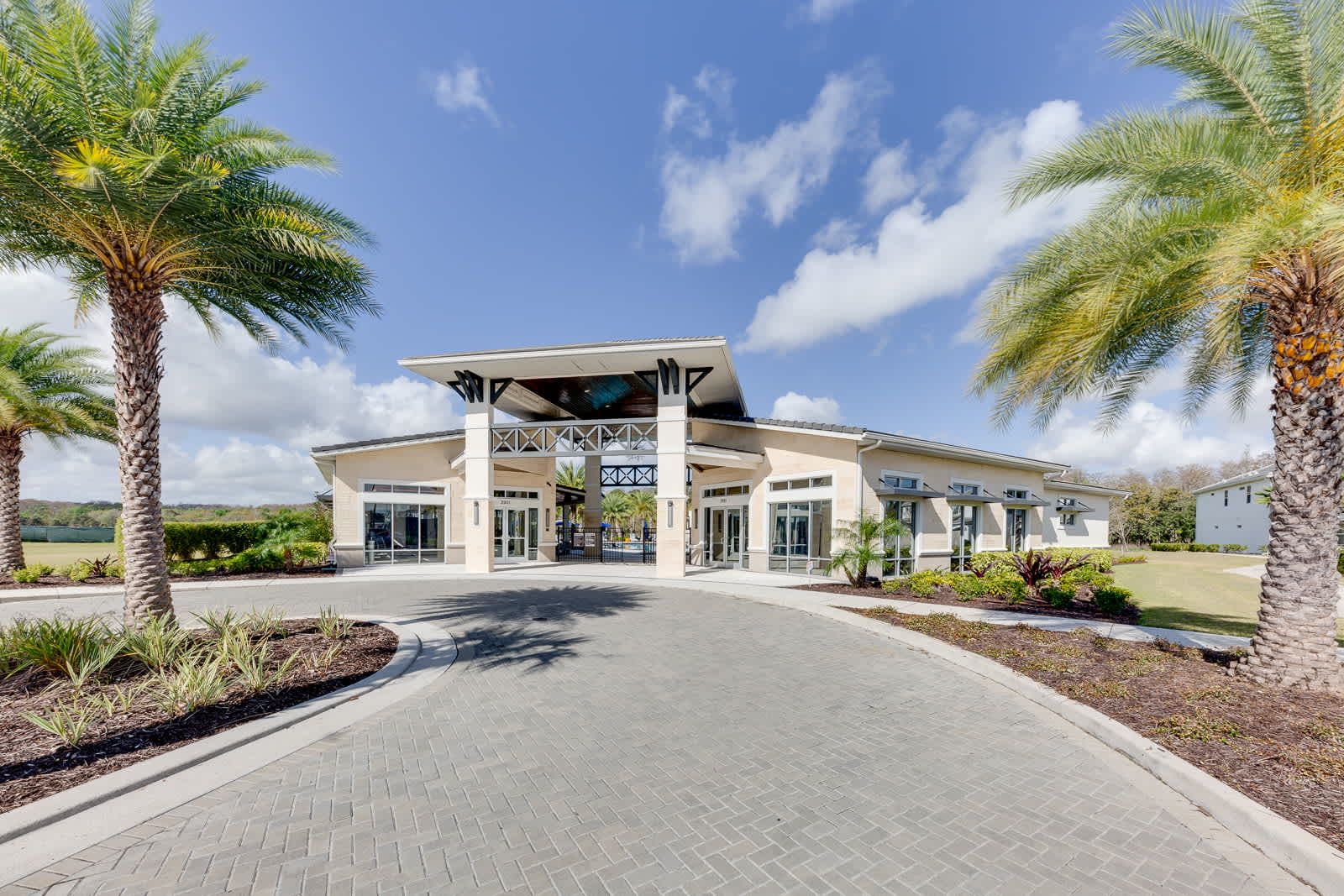 Stunning modern clubhouse entrance framed by tropical palm trees.