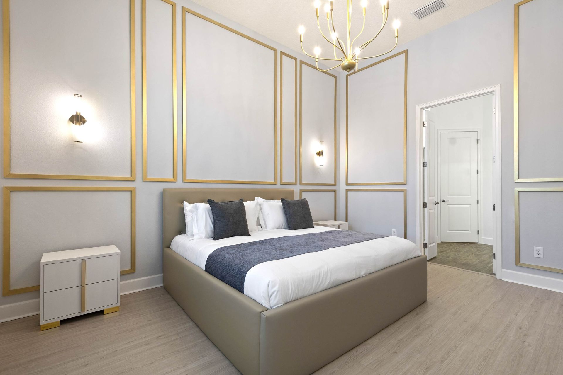 Master suite elegance: gold accent walls, plush bed, and chandelier.