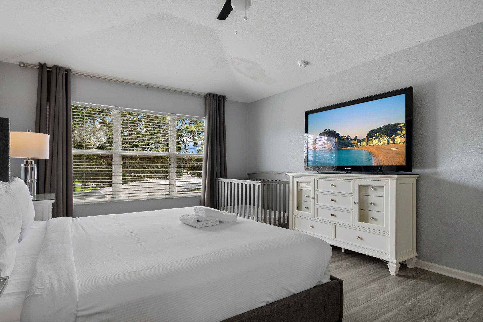 Bright master bedroom with king bed, large TV, and convenient in-room crib setup
