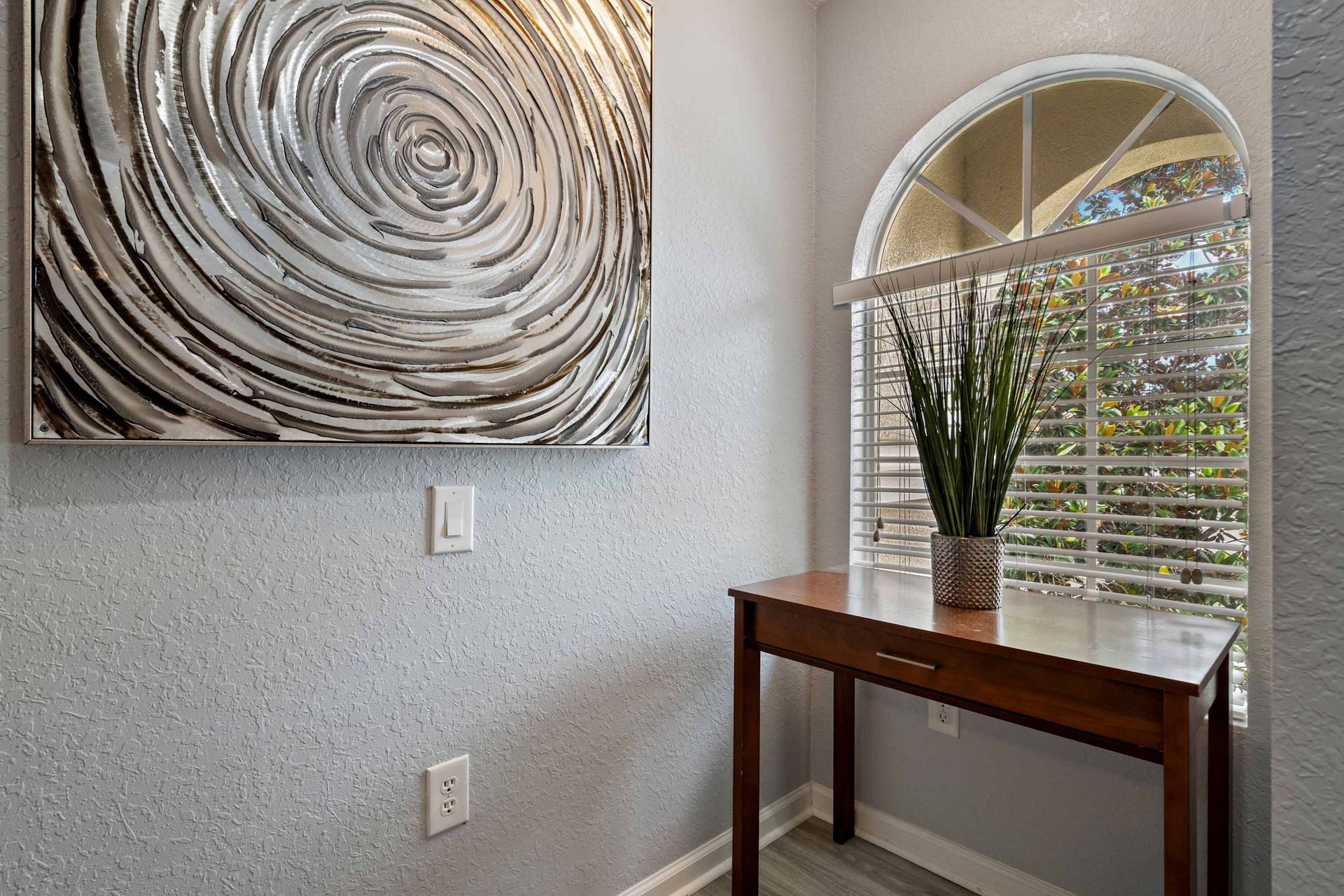 Charming hallway corner with arched window, modern art, and a decorative plant table
