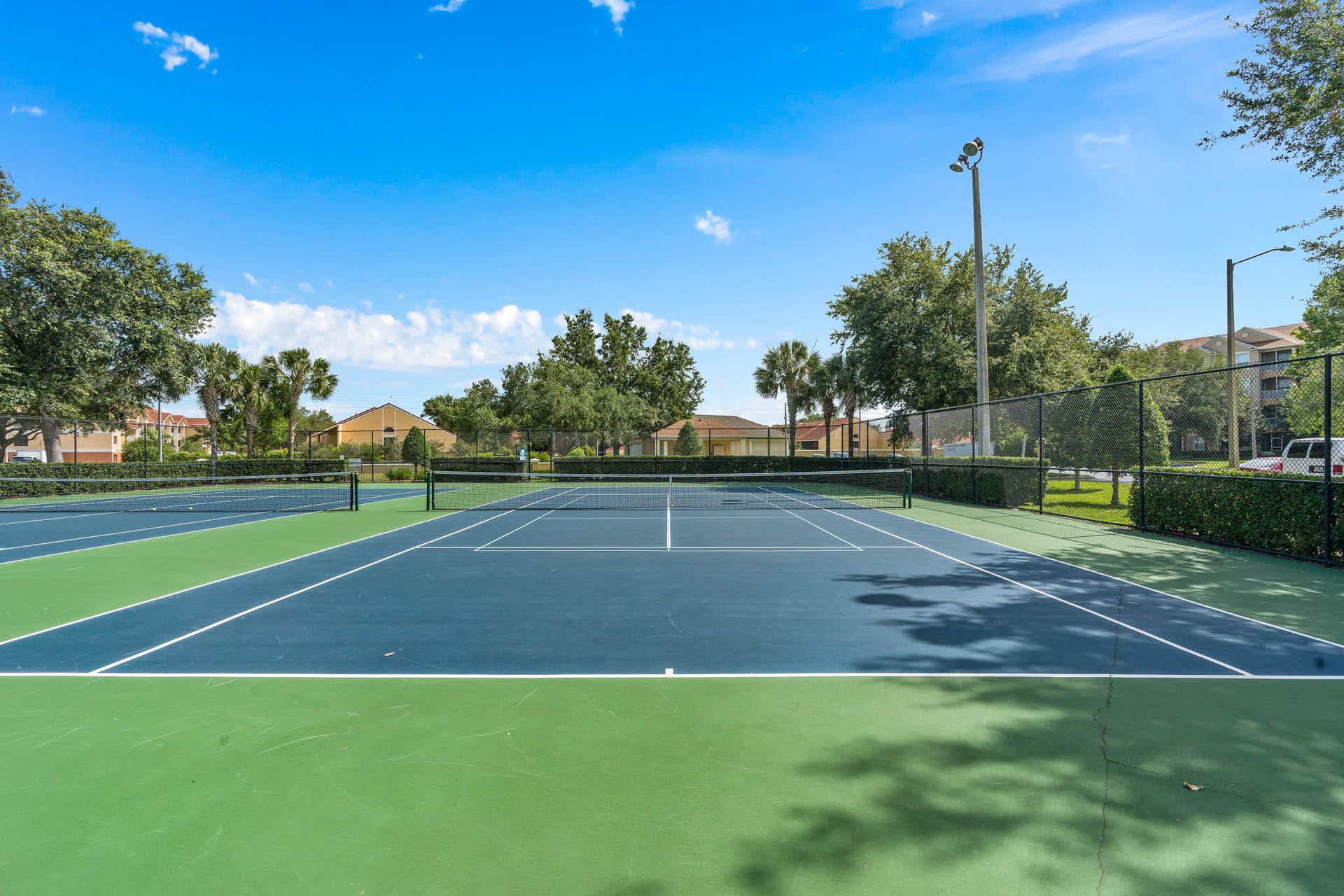 Well-maintained tennis court surrounded by lush trees and sunny skies. 