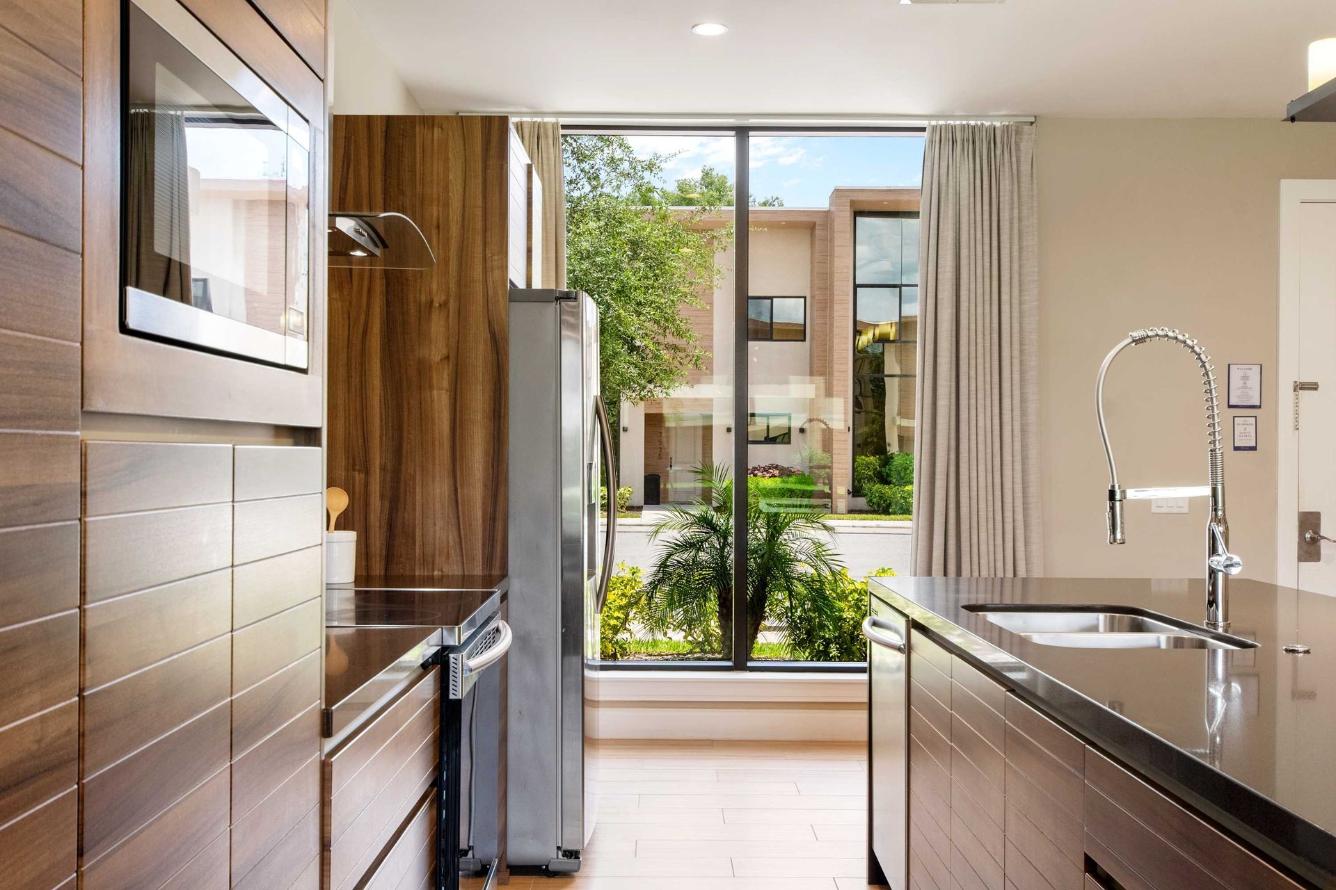 Sleek modern kitchen with rich wood grain and a sunlit garden view.