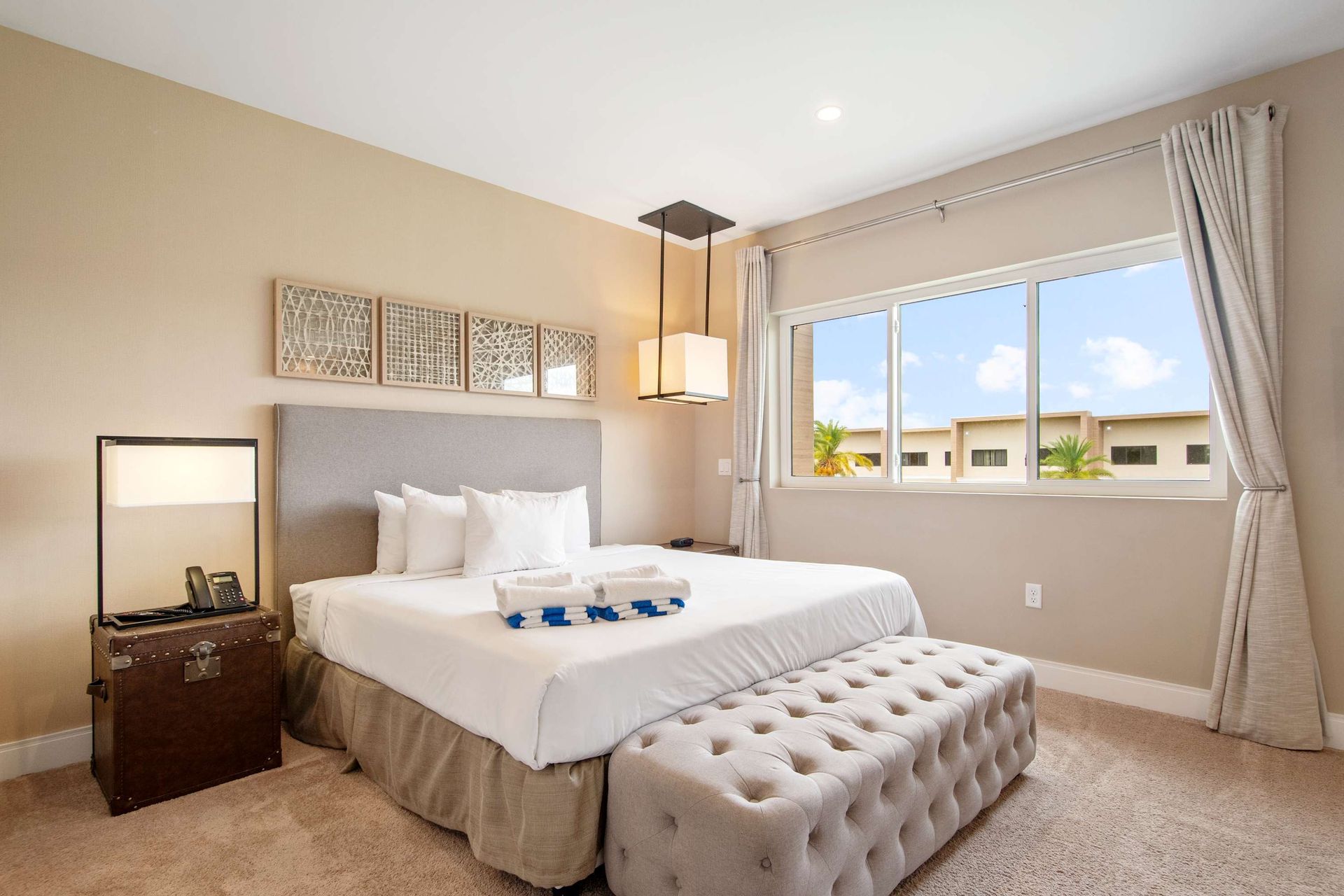 Plush King bed, tufted ottoman, and bright windows for a serene retreat.