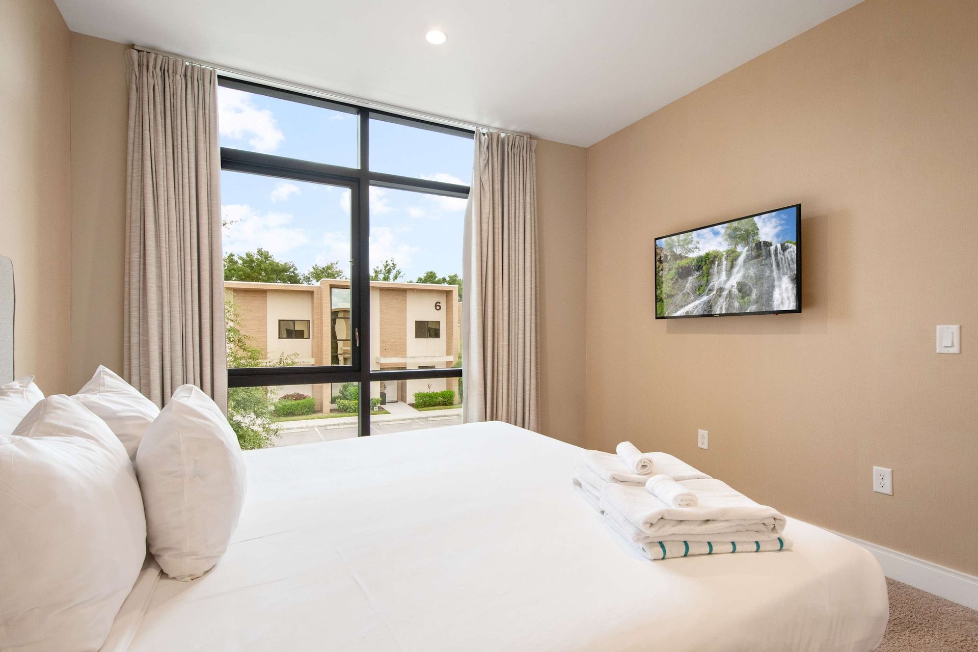 Plush Queen bed, flat-screen TV, and huge sunlit window.