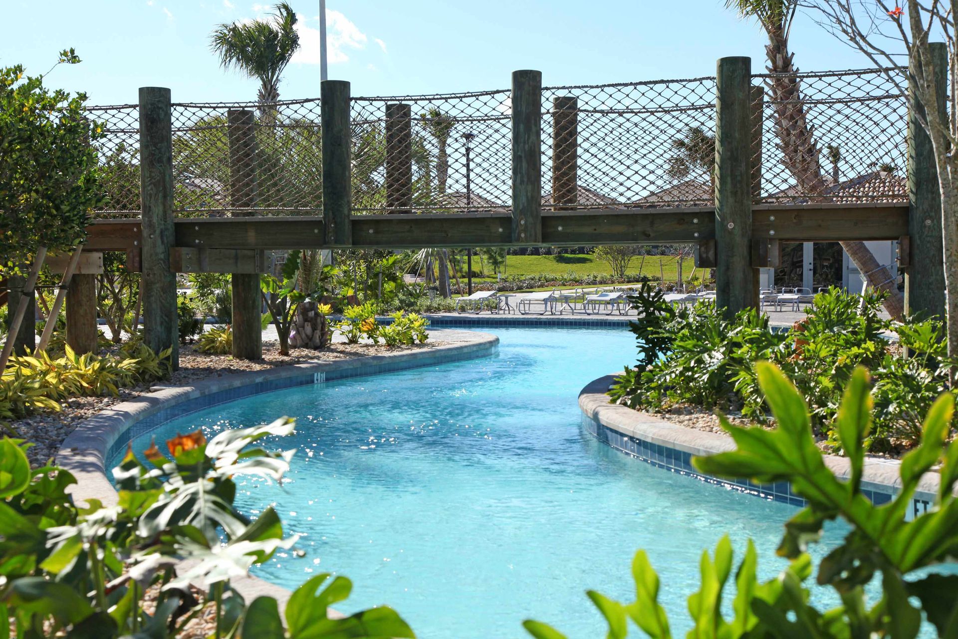 Tropical lazy river winding under a rustic rope bridge.