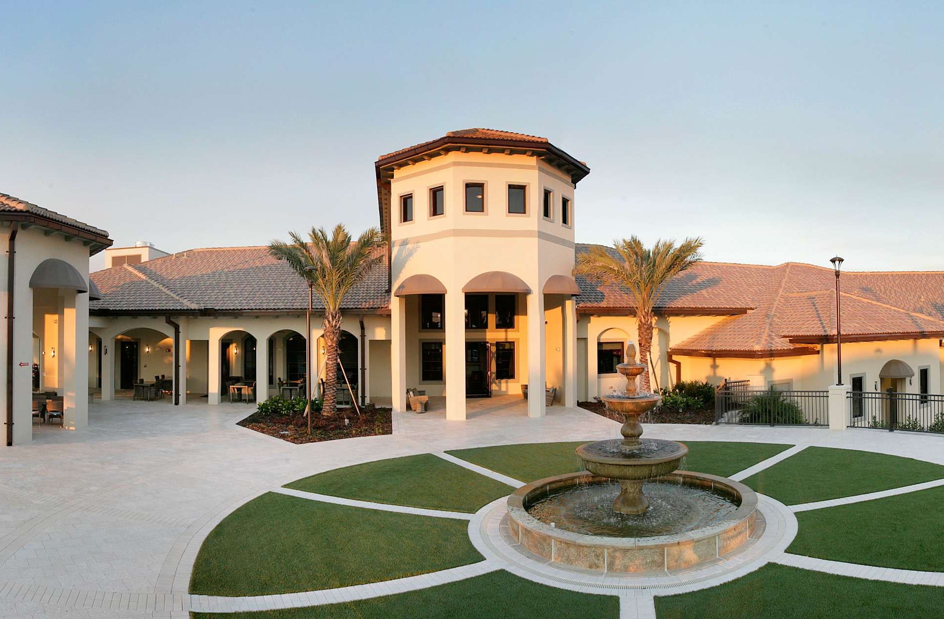 Grand resort architecture with fountain and palms at sunset.