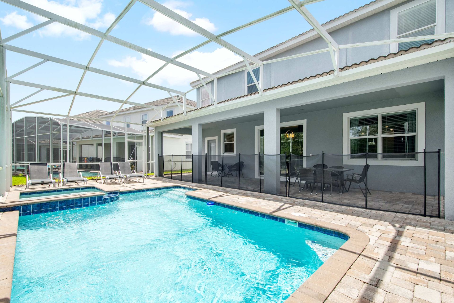 Sunny screened pool and spa with safety fence and lounge chairs.