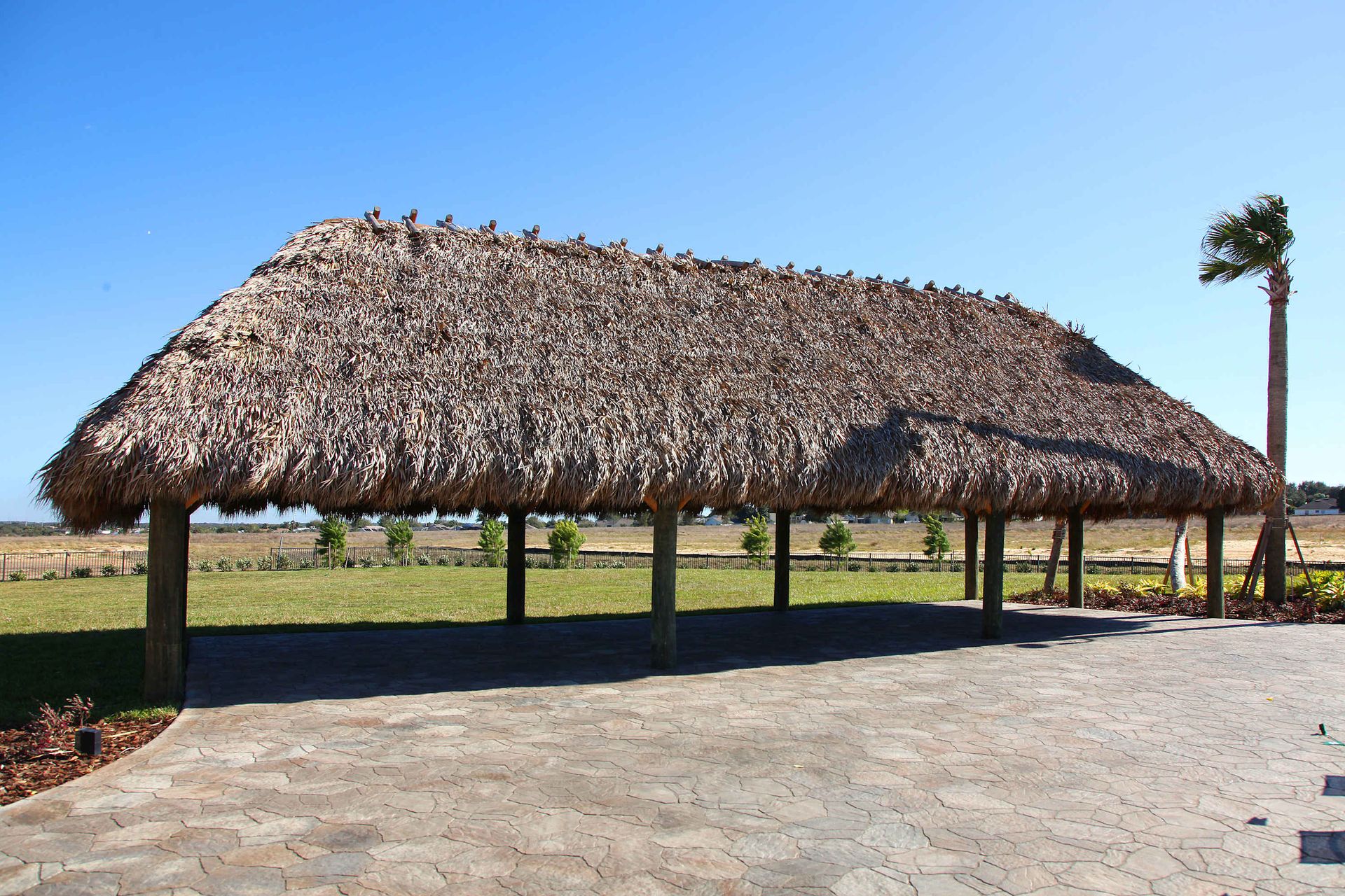 Tropical tiki hut under a bright blue sky with green grass and a palm tree.