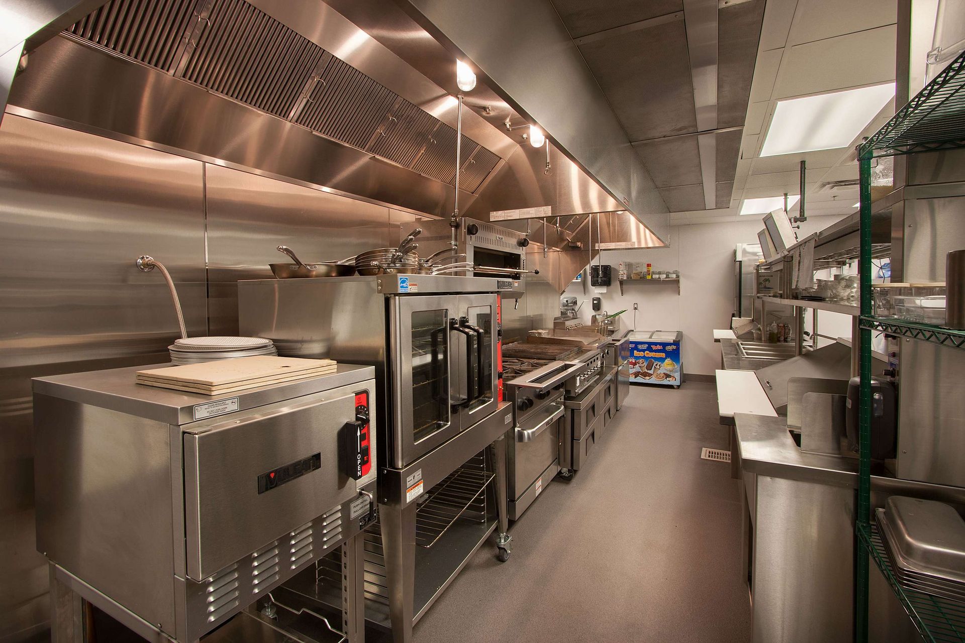 Commercial restaurant kitchen with stainless steel equipment, hood vents, and racks.