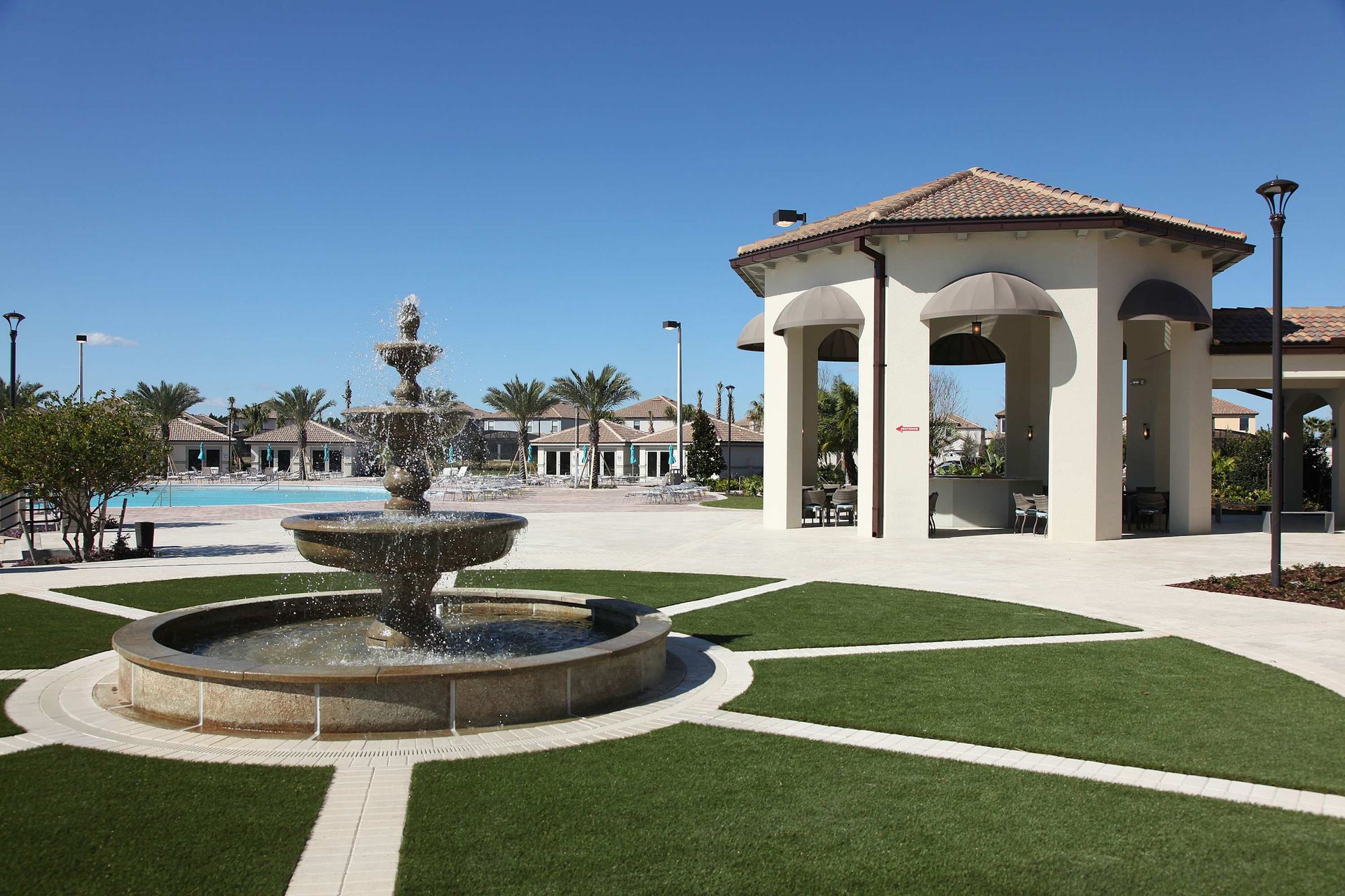 Tiered water fountain, gazebo, lawn, and pool area under a clear sky.