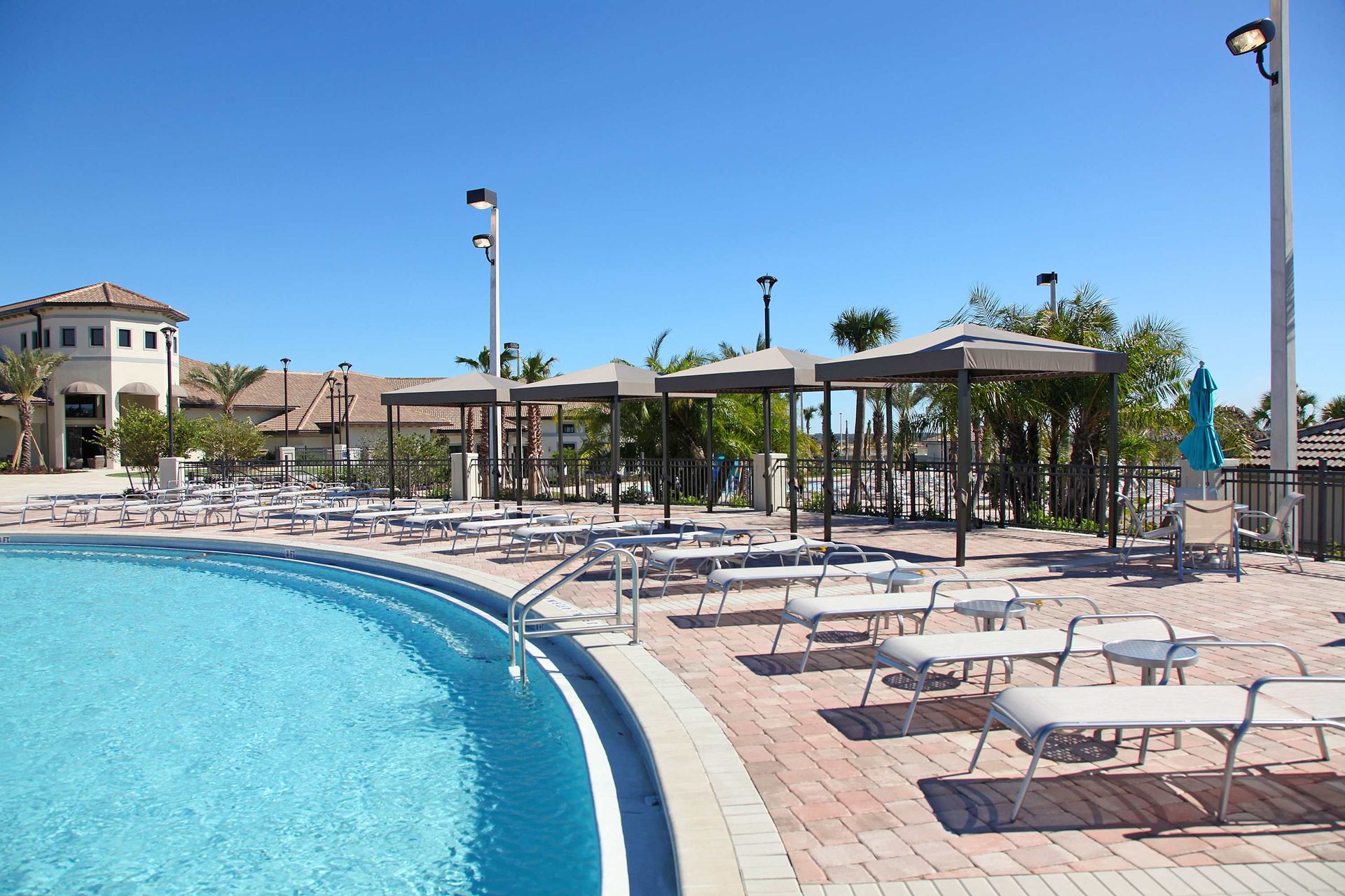 Bright, sunny pool scene with vibrant blue water and a Mediterranean-style building.
