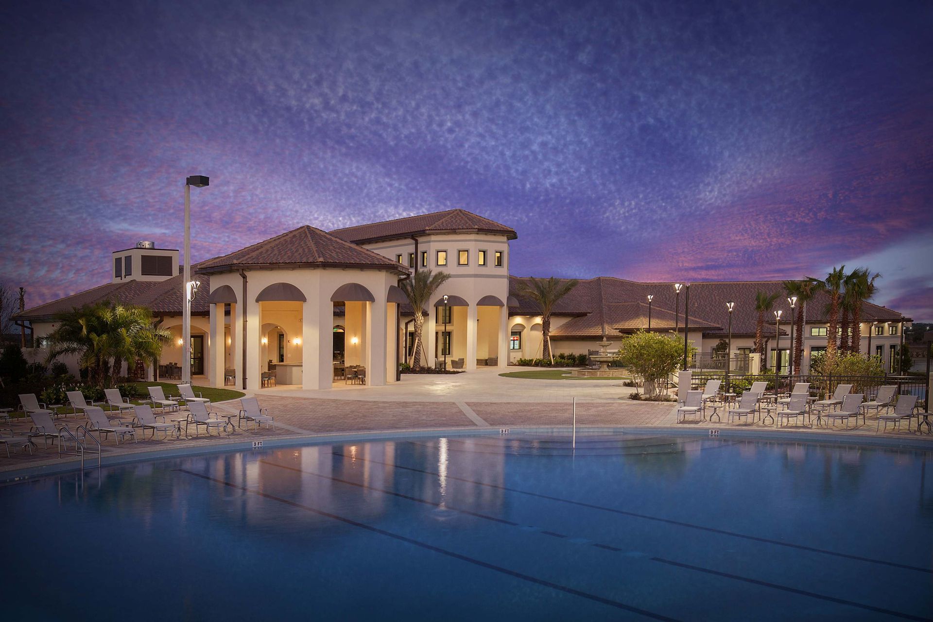 Clubhouse building, large pool, and lounge chairs under a dramatic dusk sky.