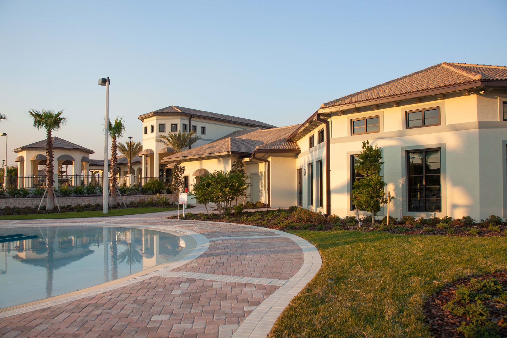 Clubhouse building, curved pool edge, paved walkway, and palm trees.